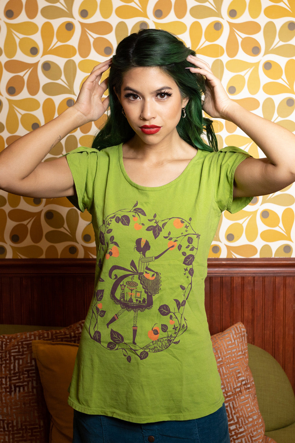 Model wearing green tee with graphic of girl pciking orange apples