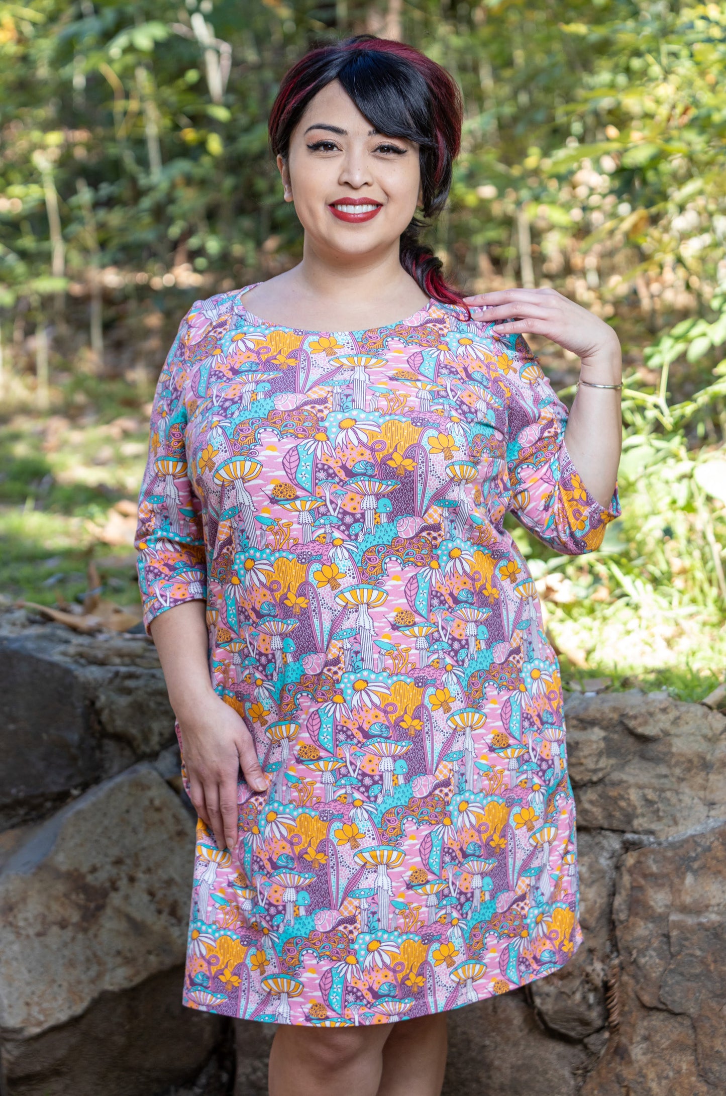 Model wearing pink, yellow and aqua pocket tunic with mushrooms, flowers and snails