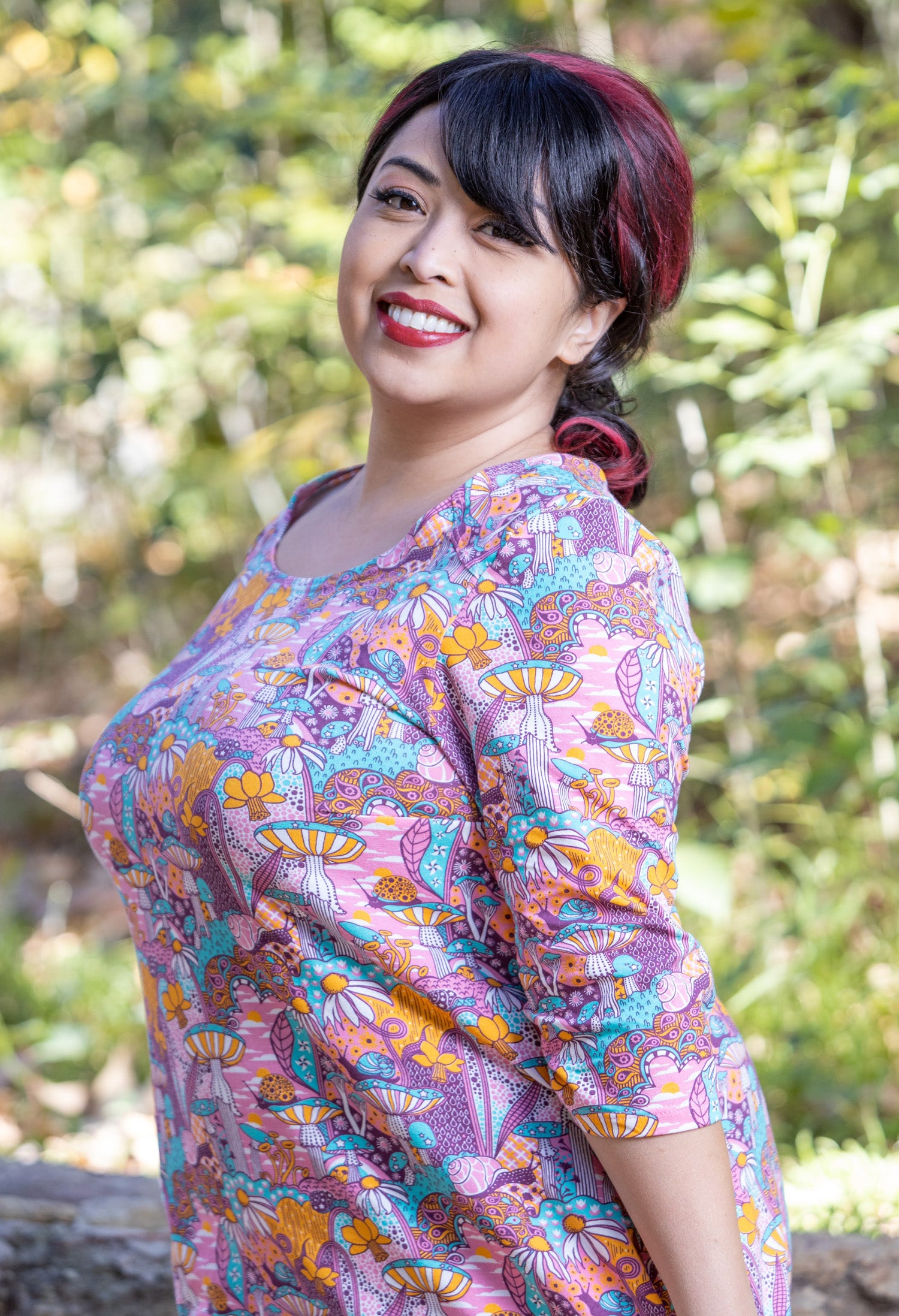 Side view closeup of model wearing pink, yellow and aqua pocket tunic with mushrooms, flowers and snails
