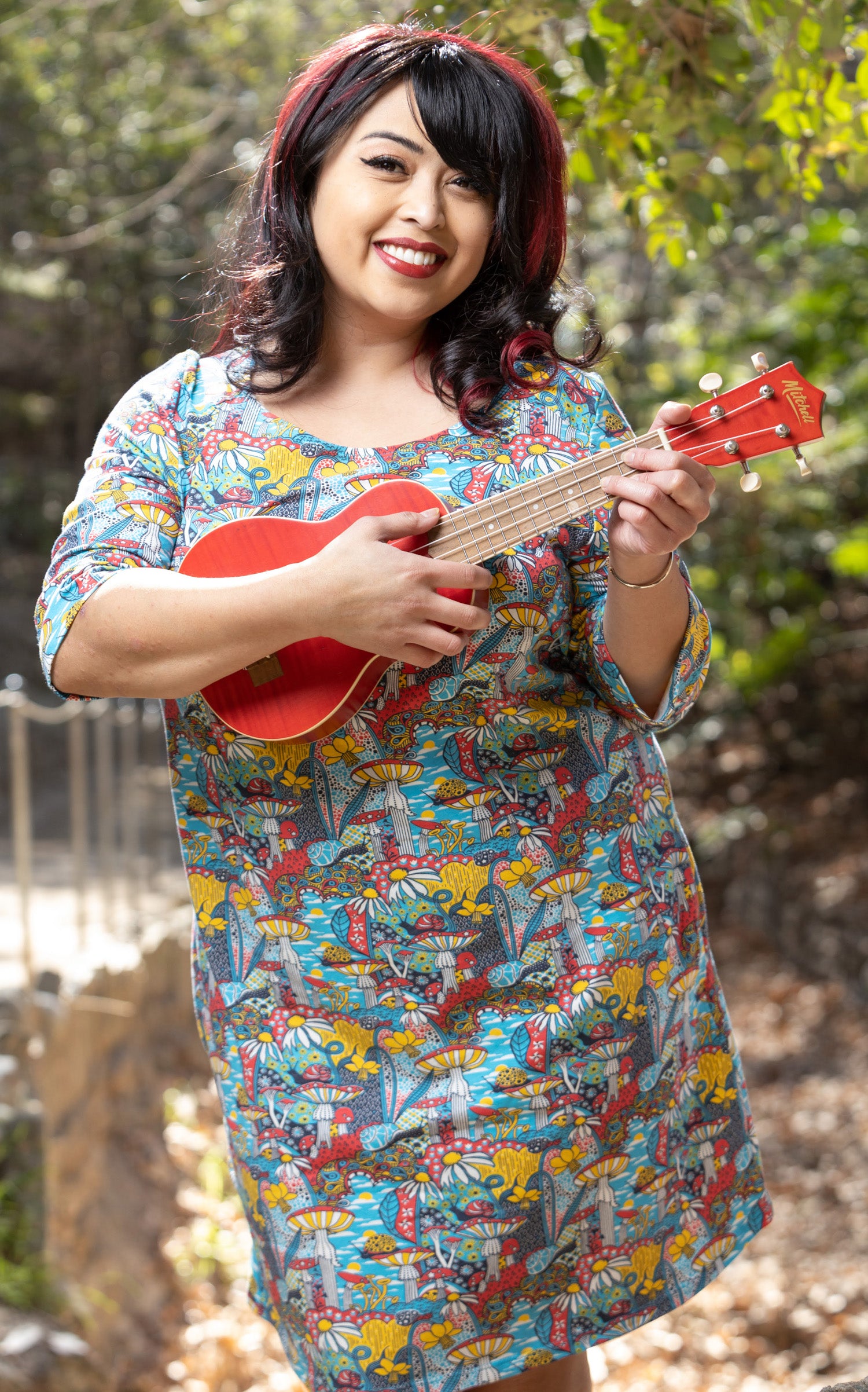 Model holding guitar wearing tunic with colorful fantasy landscape featuring mushrooms