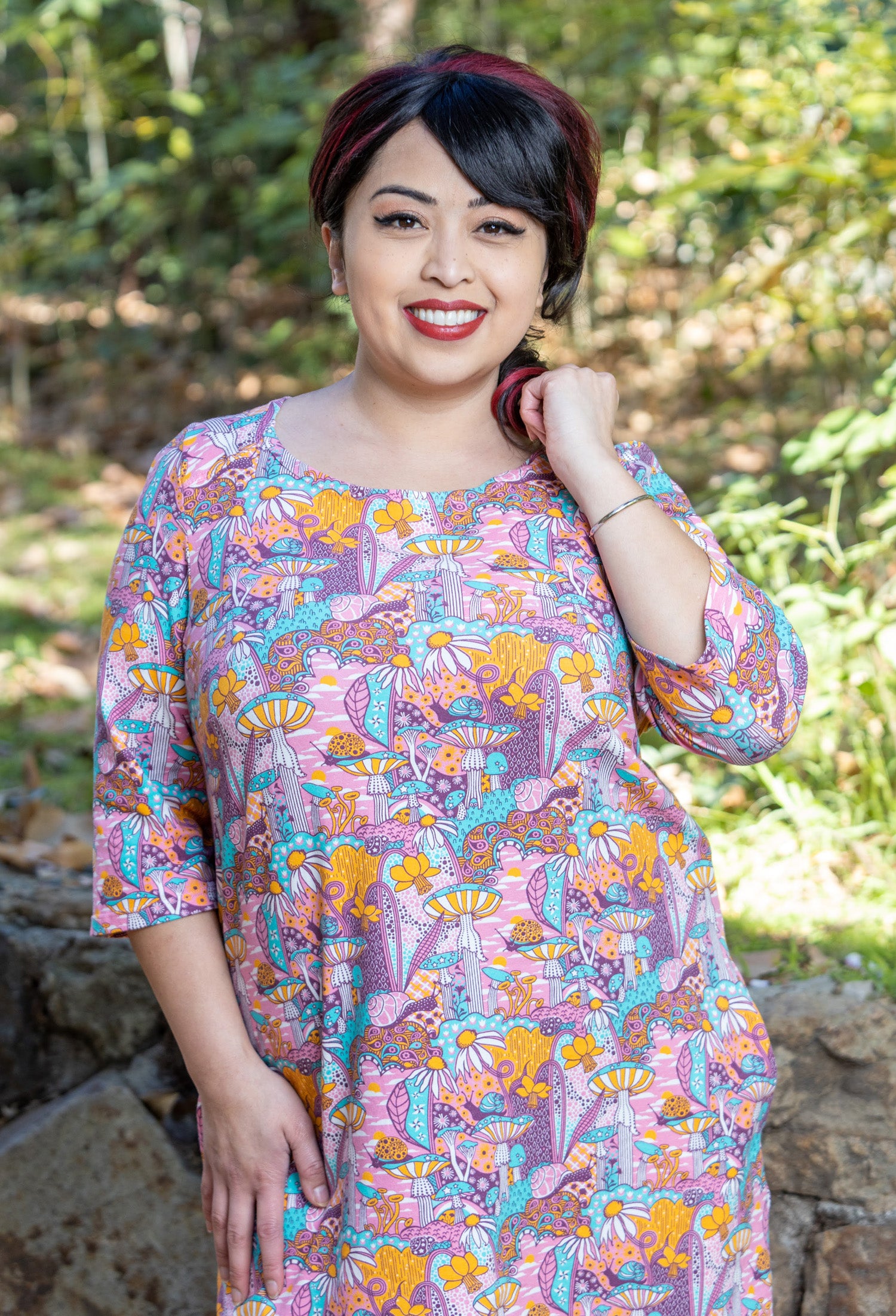 Model wearing pink, yellow and aqua pocket tunic with mushrooms, flowers and snails
