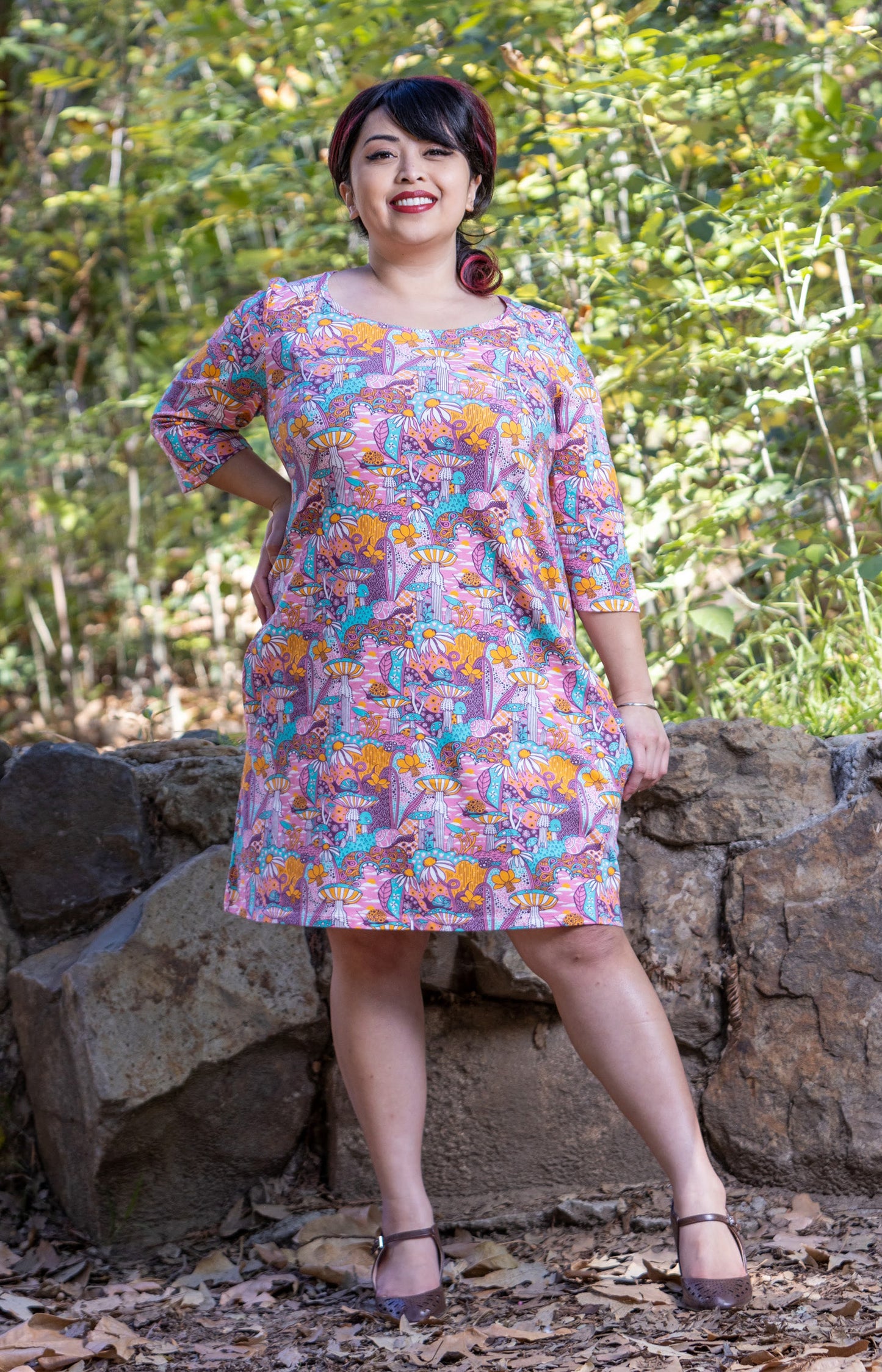 Model wearing pink, yellow and aqua pocket tunic with mushrooms, flowers and snails