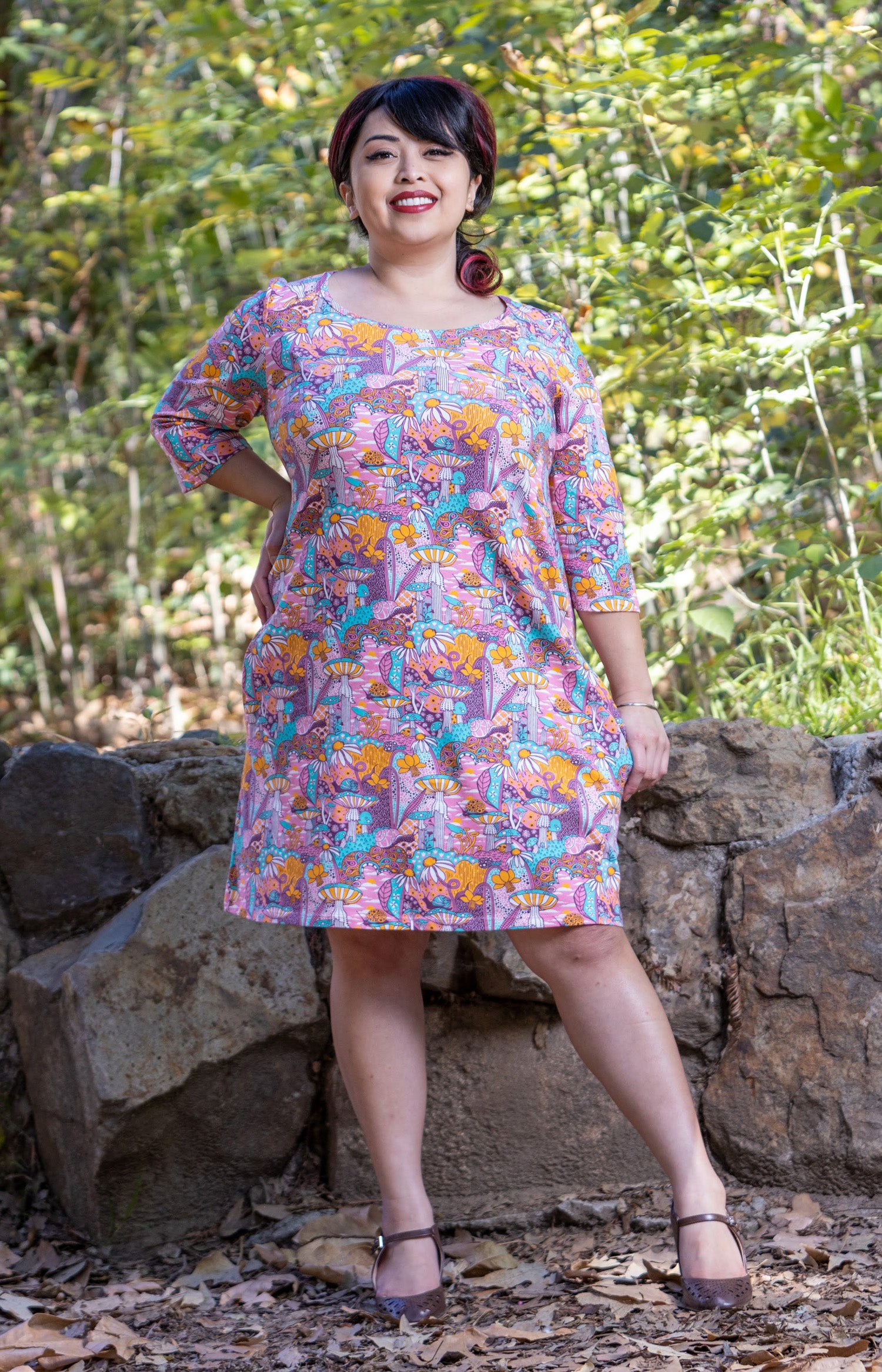 Model wearing pink, yellow and aqua pocket tunic with mushrooms, flowers and snails