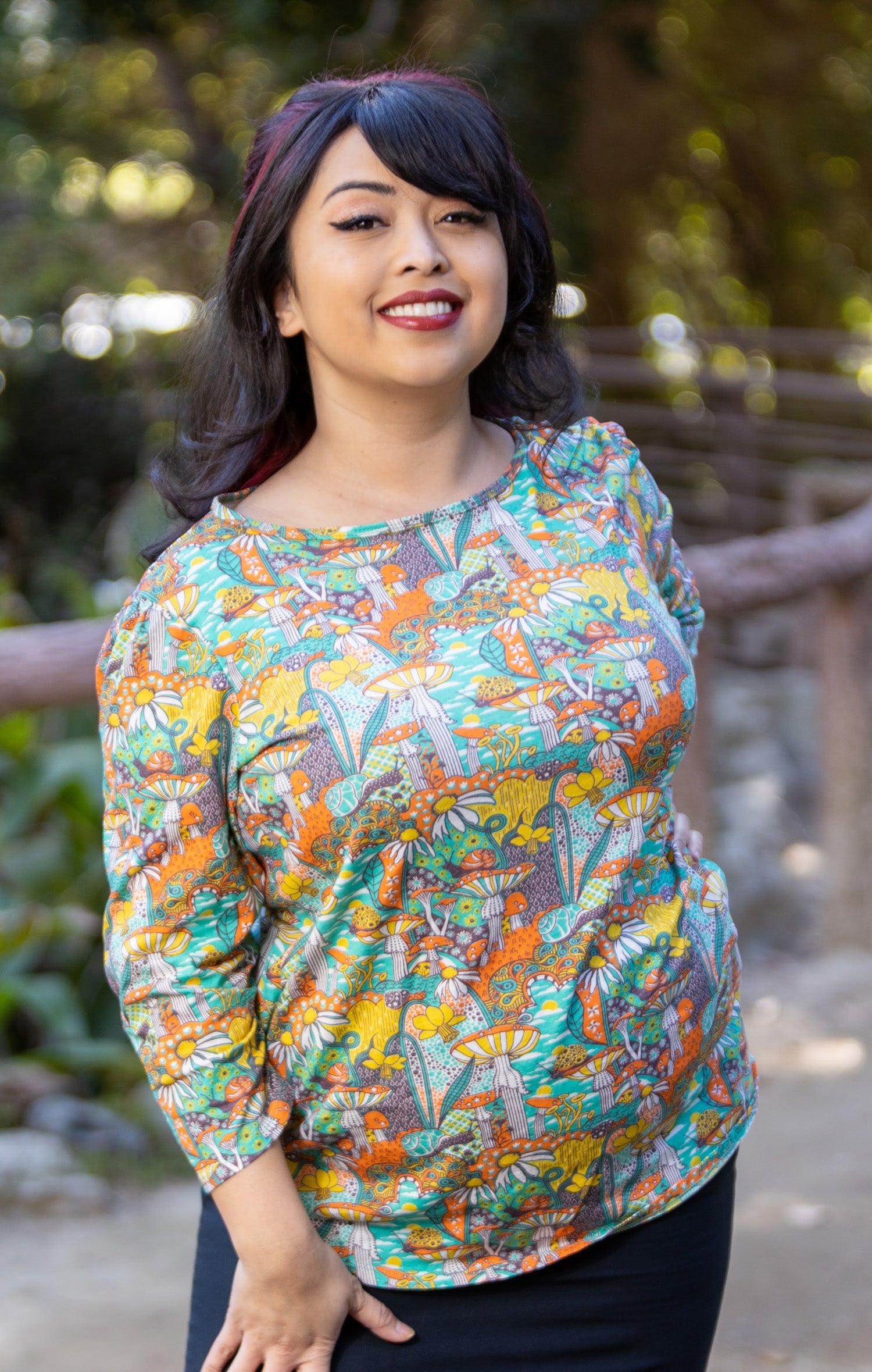 Model wearing 3/4 sleeve shirt featuring colorful fantasy landscape and mushrooms