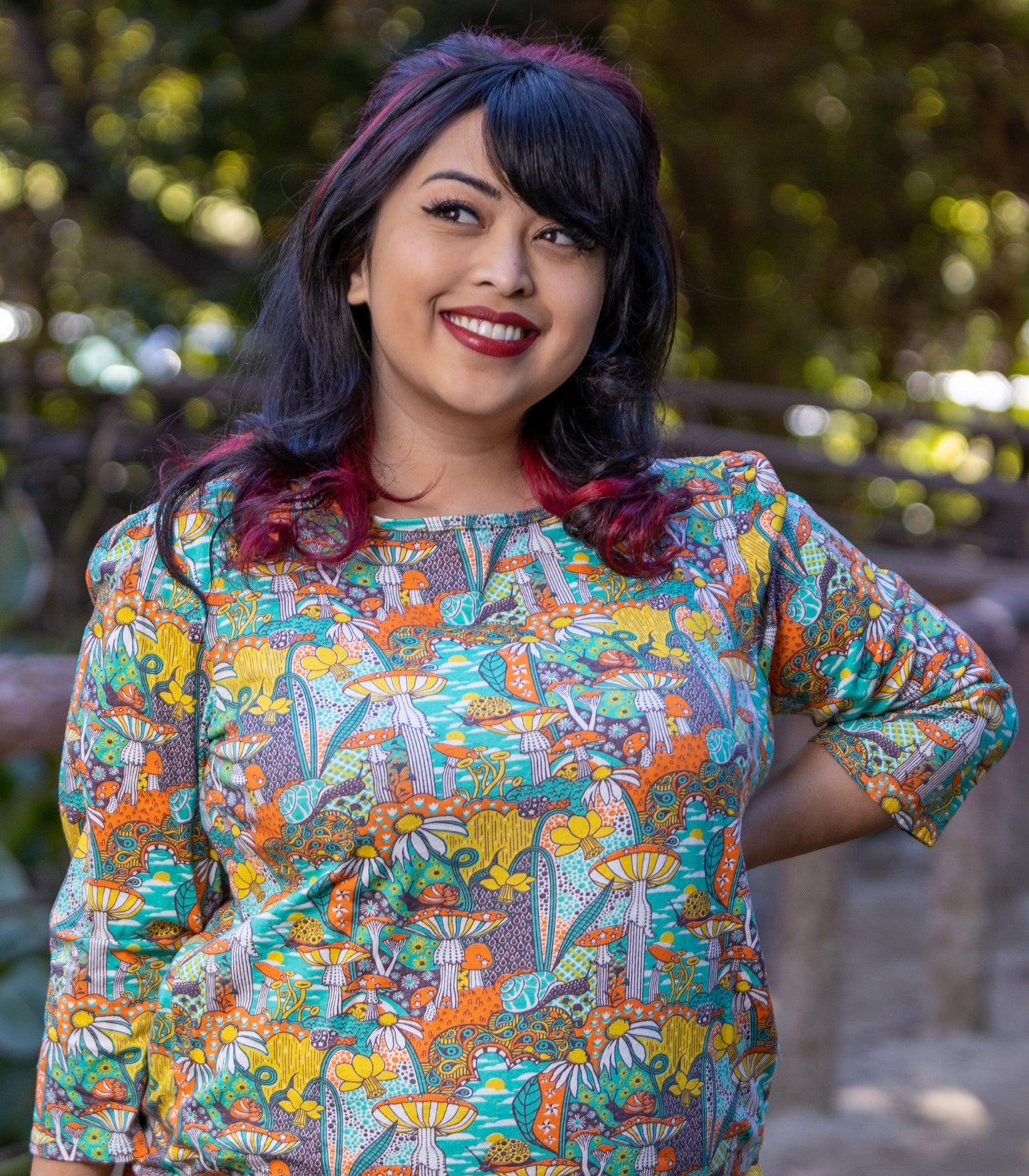 Model wearing 3/4 sleeve shirt featuring colorful fantasy landscape and mushrooms