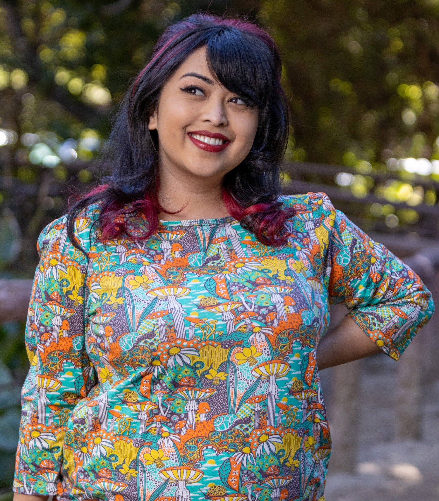 Model wearing 3/4 sleeve shirt featuring colorful fantasy landscape and mushrooms