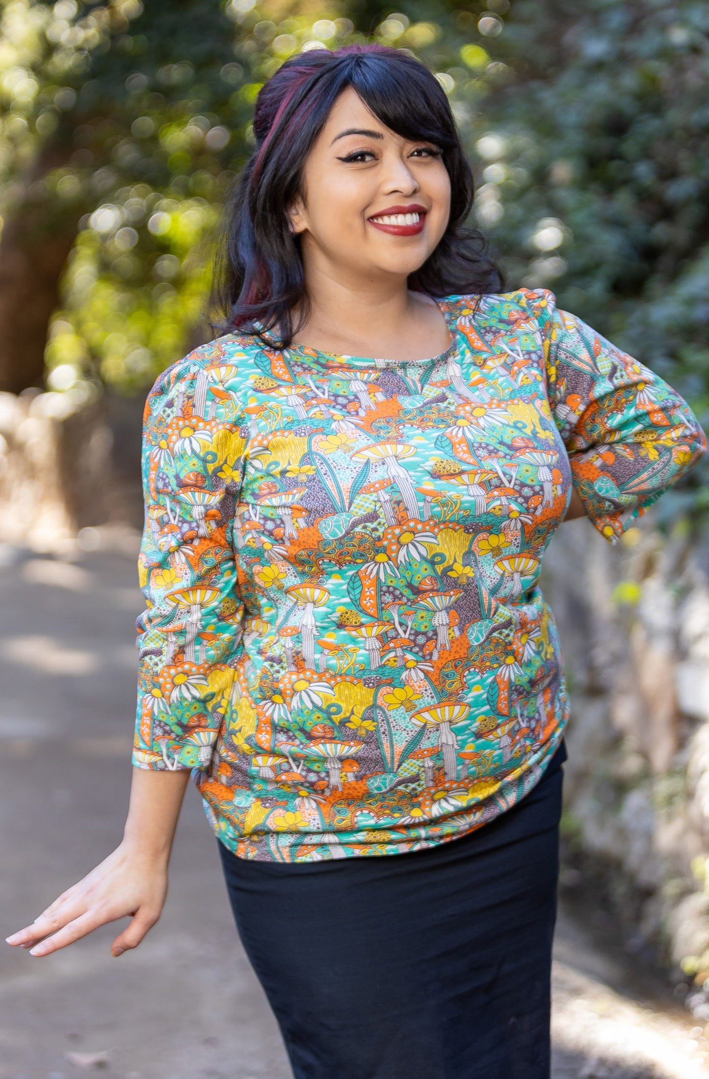 Model wearing 3/4 sleeve shirt featuring colorful fantasy landscape and mushrooms