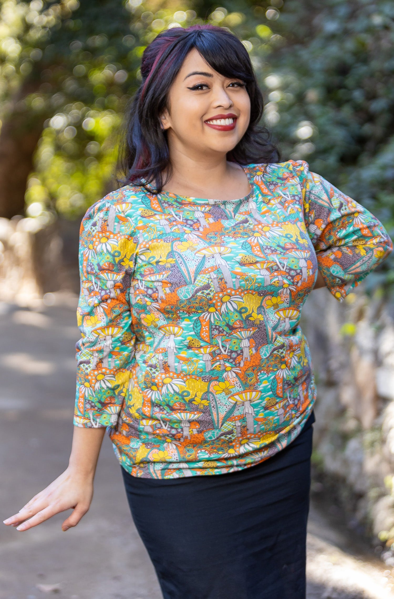 Model wearing 3/4 sleeve shirt featuring colorful fantasy landscape and mushrooms