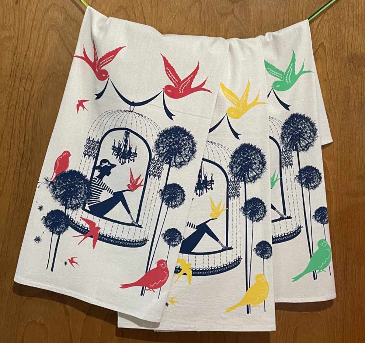 3 colorful cotton tea towels with birds and a woman in a birdcage on wood background