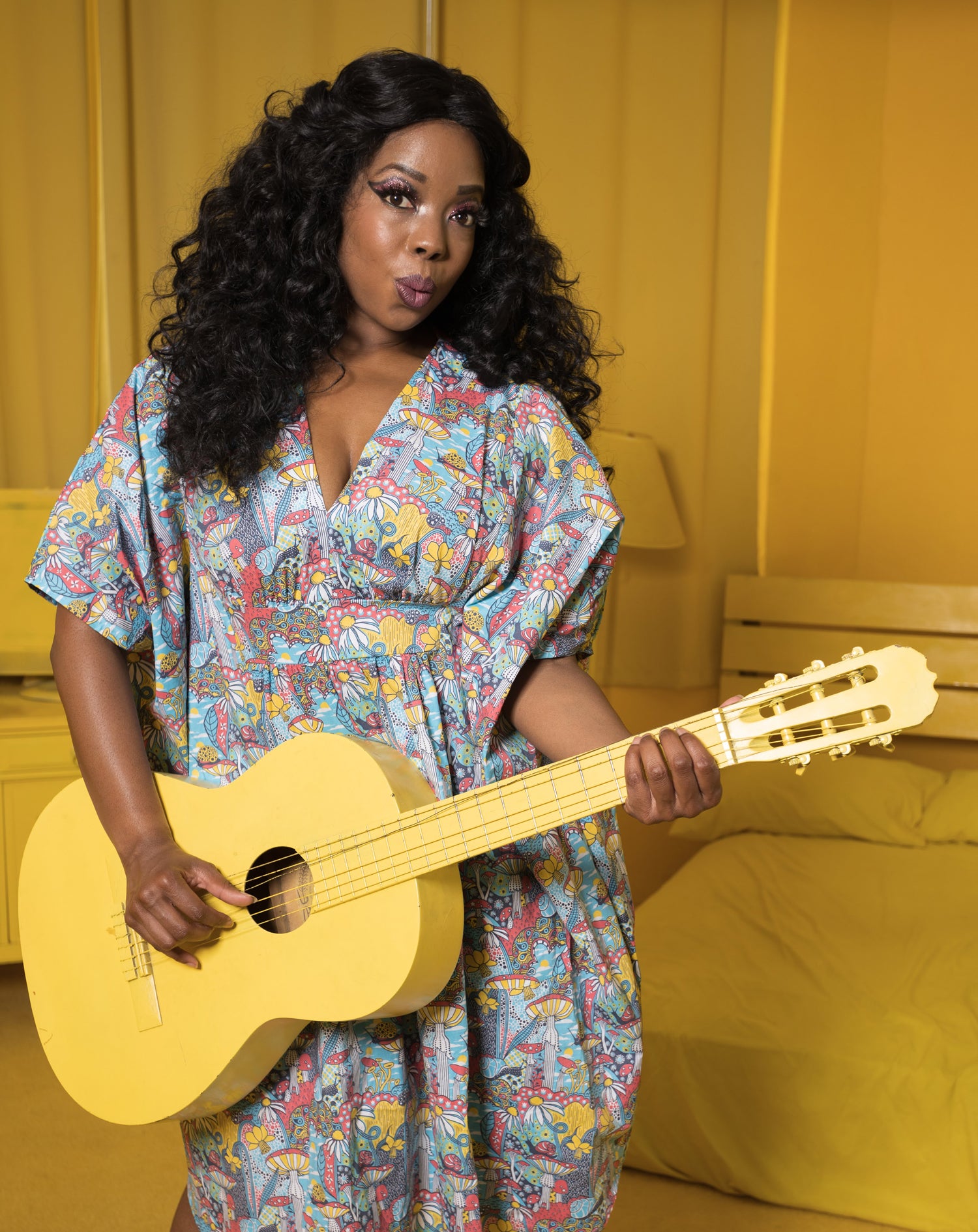 V-neck aqua, red and yellow mushroom, snail, and flower print midi caftan dress on model holding guitar in yellow room