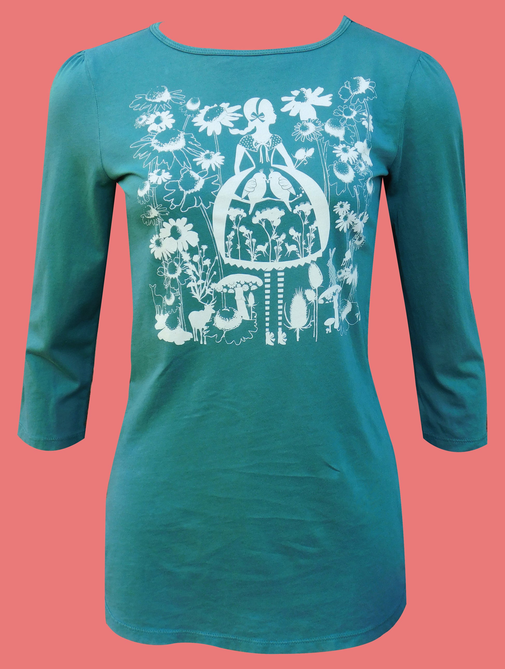 Model wearing dark green sweatshirt with screen print of birch trees, leaves, birds and deer on peach backdrop