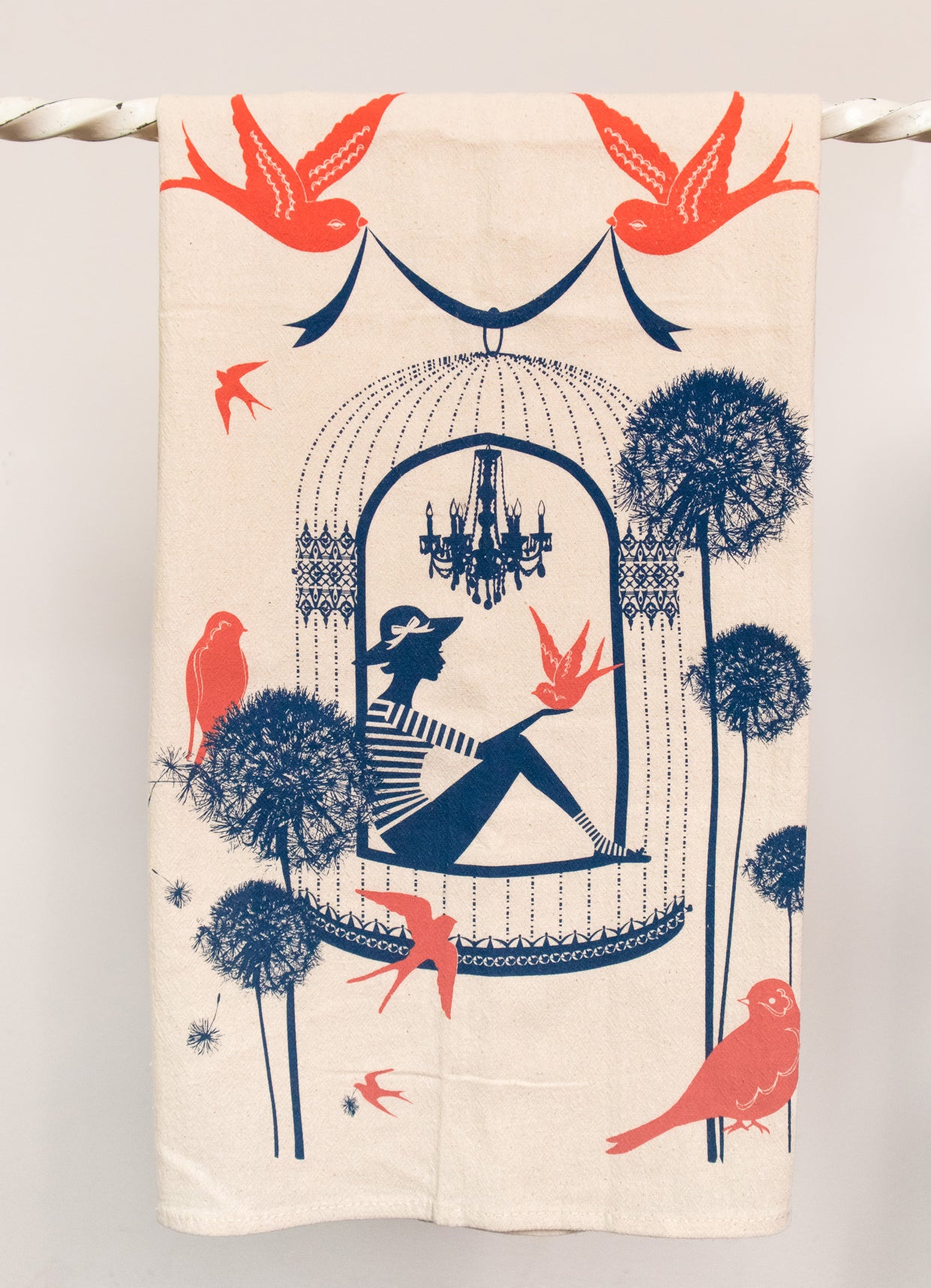 Cotton tea towel with bright coral and navy print of a woman in a birdcage with birds and flowers