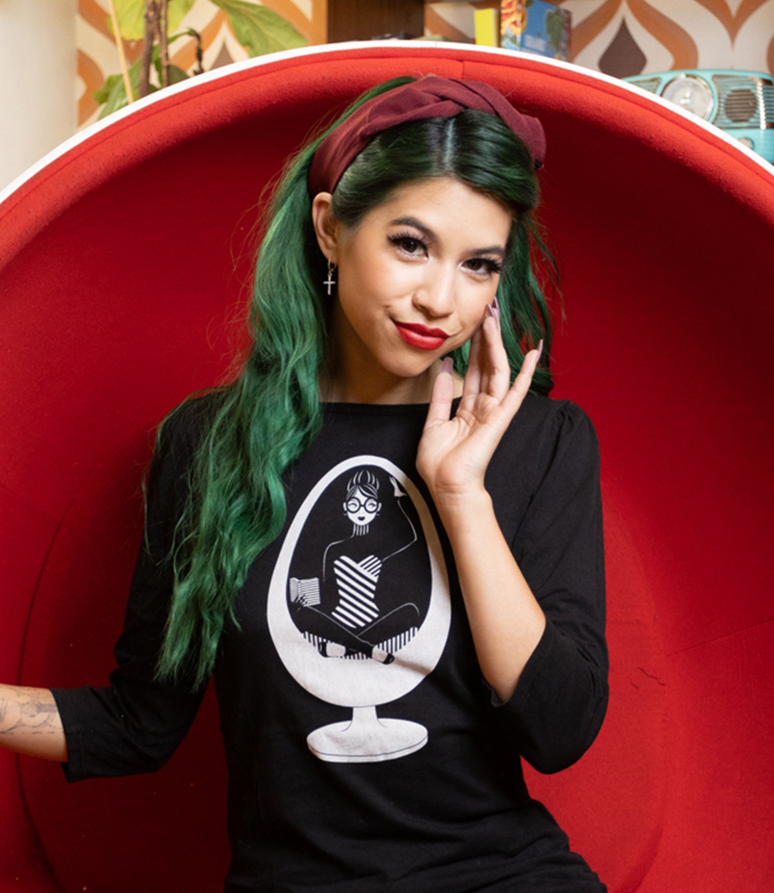 Closeup of long-haired girl wearing black 3/4 sleeve tee with white graphic of girl reading in a vintage egg chair