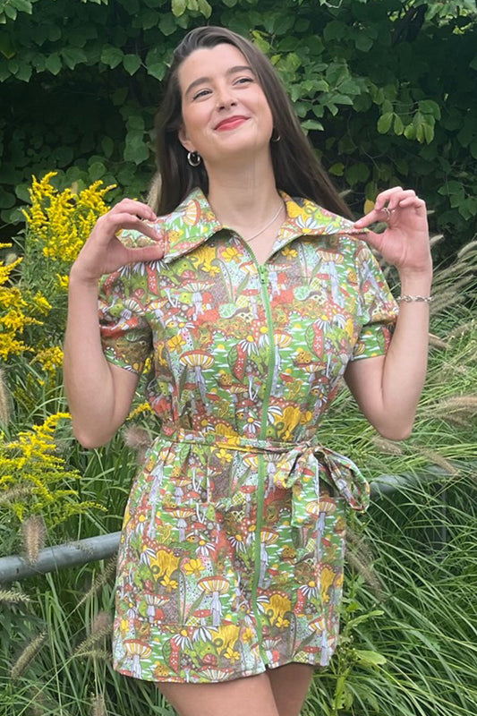 Dark haired model wearing olive minidress with mushroom and flower graphic print