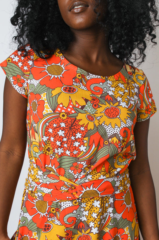 Orange yellow and green daisy and tulip print maxi dress with pockets and a twist belt detail worn by  model.