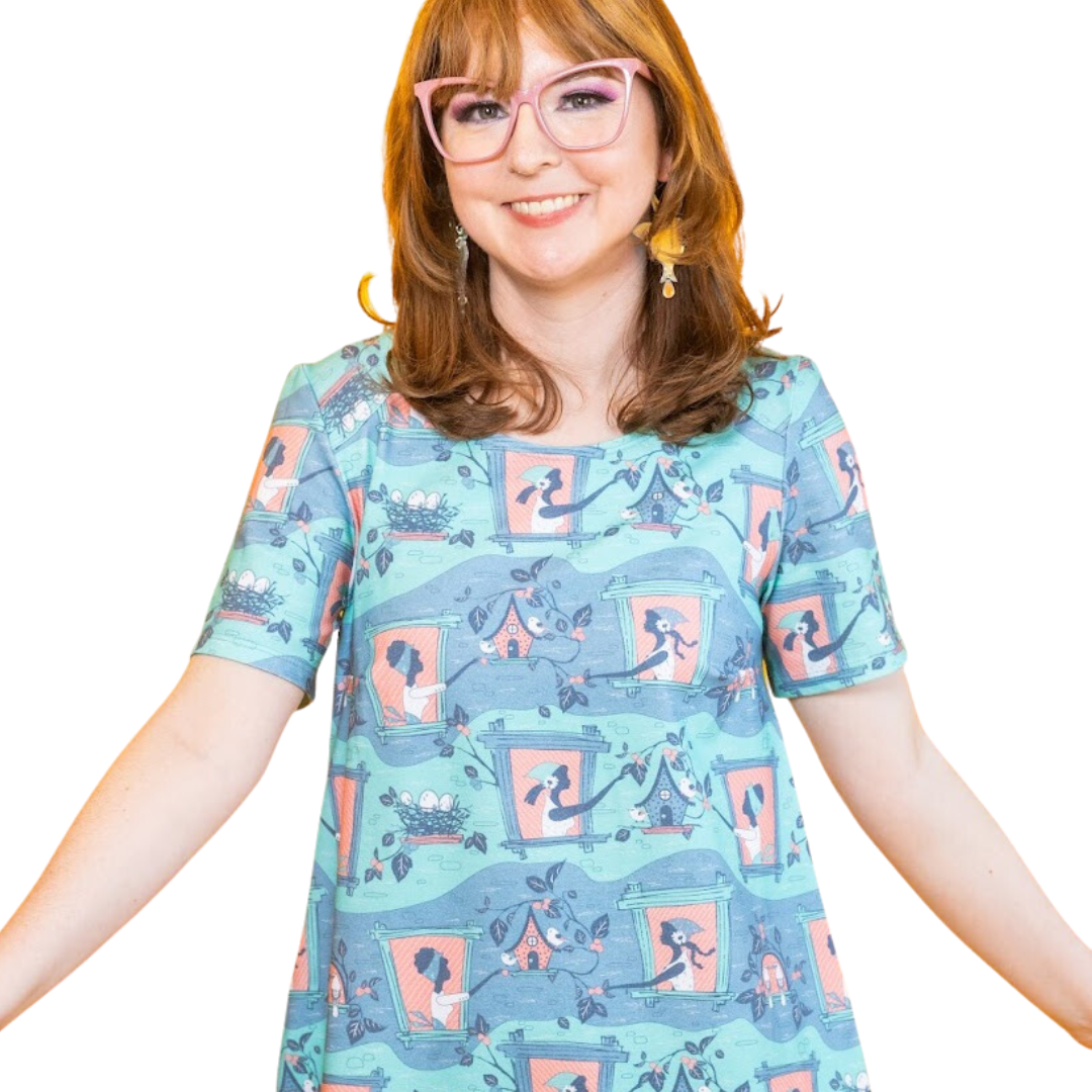 Closeup of model in tunic featuring girl and birdhouse print in peach and aqua