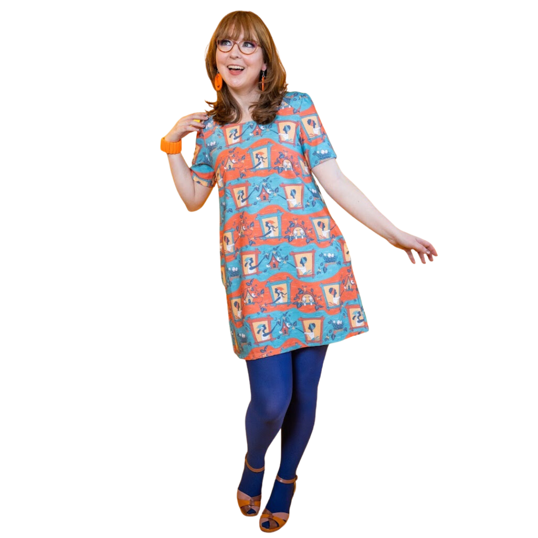 Model in red, blue and yellow pocket tunic with cute print of girls in windows feeding the birds and picking berries