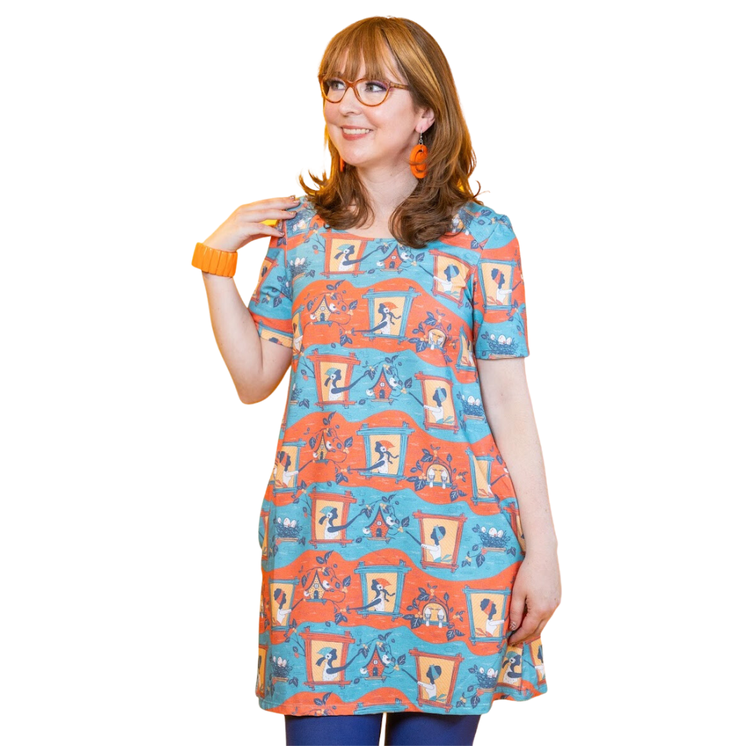 Girl in glasses wearing tunic featuring girls in windows feeding birds and picking berries