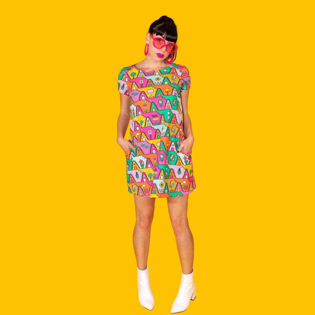 Dark-haired model in bright multicolored geometric pocket tunic with ankle boots and bright pink sunglasses