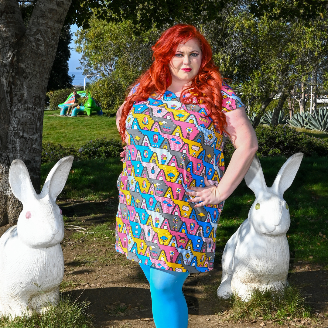 Gorgeous red-haired model posing in pastel colored geometric tunic in pink, yellow and blue, surrounded by bunny statues