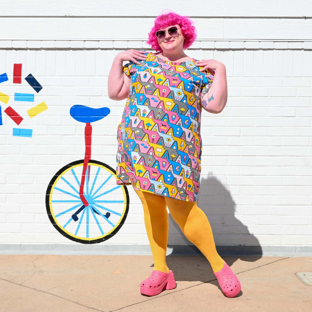 Pink-haired model in pastel print tunic, standing in front of fun painted wall