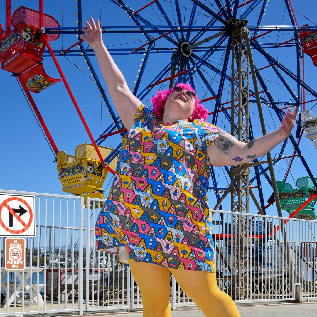 Fun pink-haired model posing in geometric print tunic in front of a ferris wheel