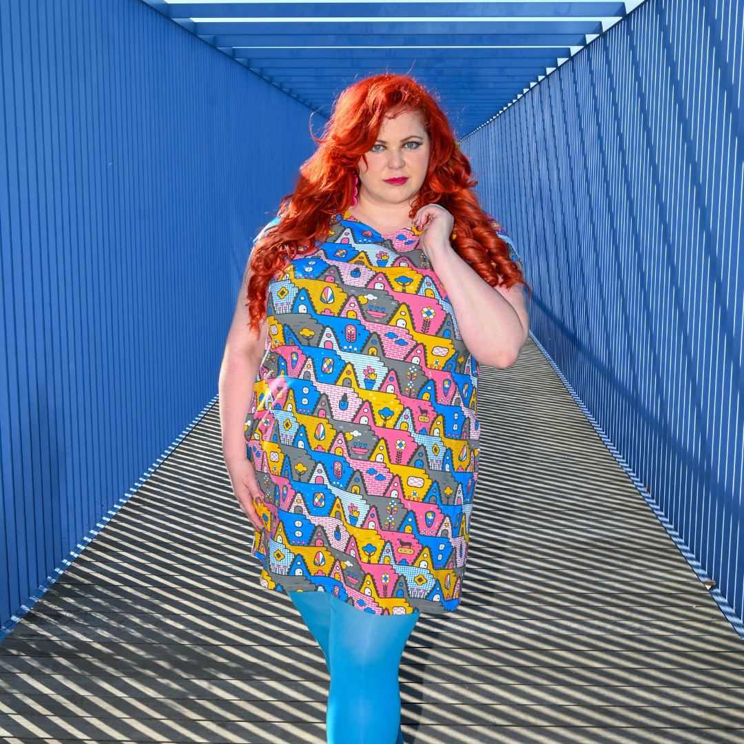 Red-haired model wearing geometric a-frame print tunic, posing in a tunnel