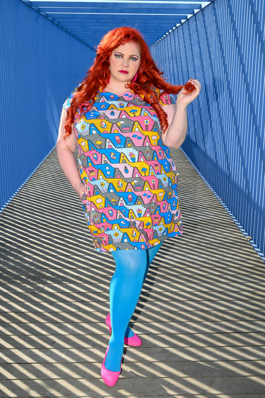 Gorgeous red-haired model posing in pastel colored geometric tunic in pink, yellow and blue in a tunnel