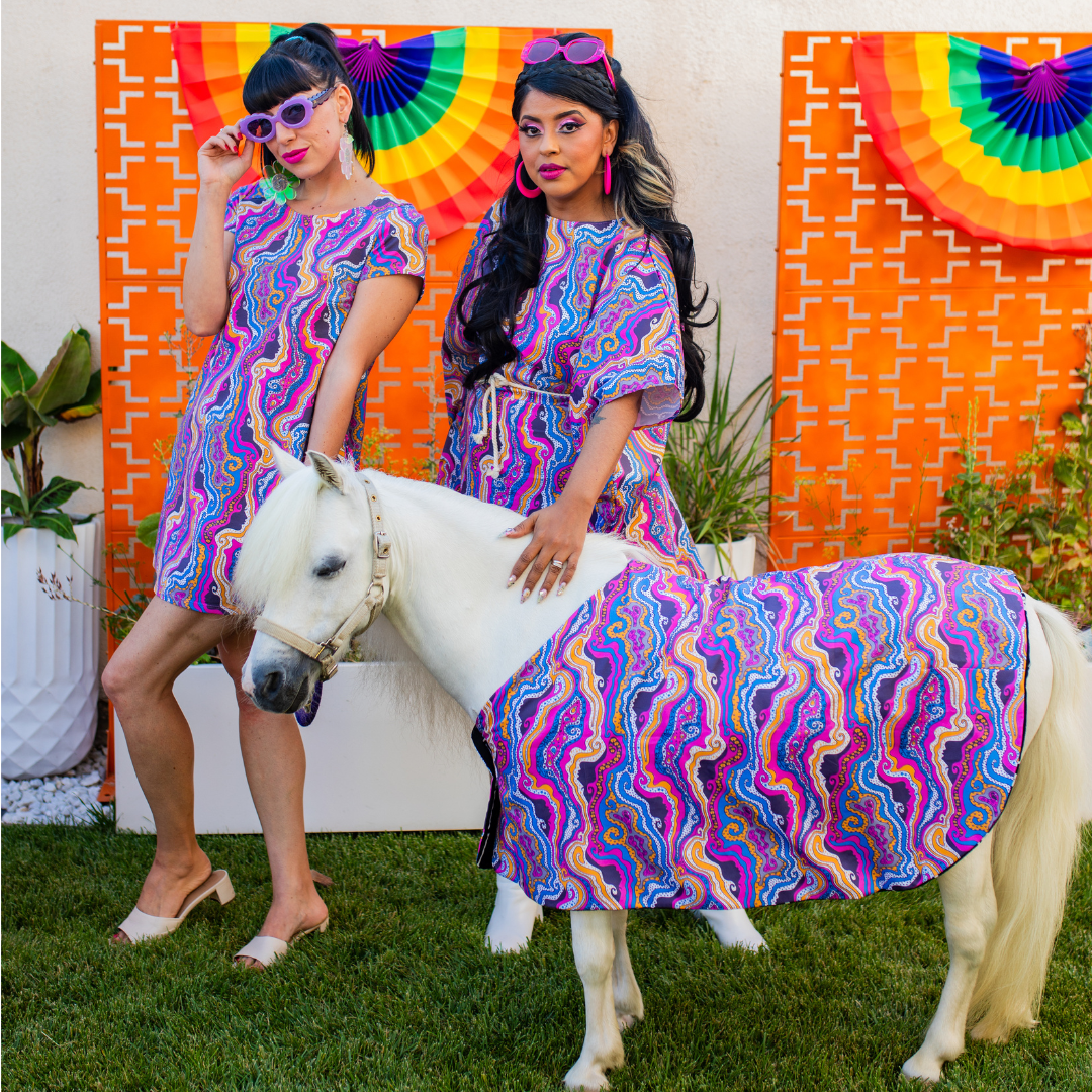 2 pretty models in gorgeous bright psychedelic dresses and white minihorse in matching blanket