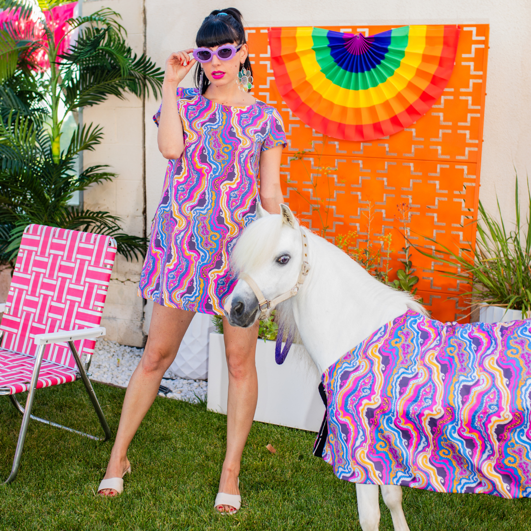 Tall dark-haired model in colorful psychedelic mini tunic dress with minihorse in matching outfit