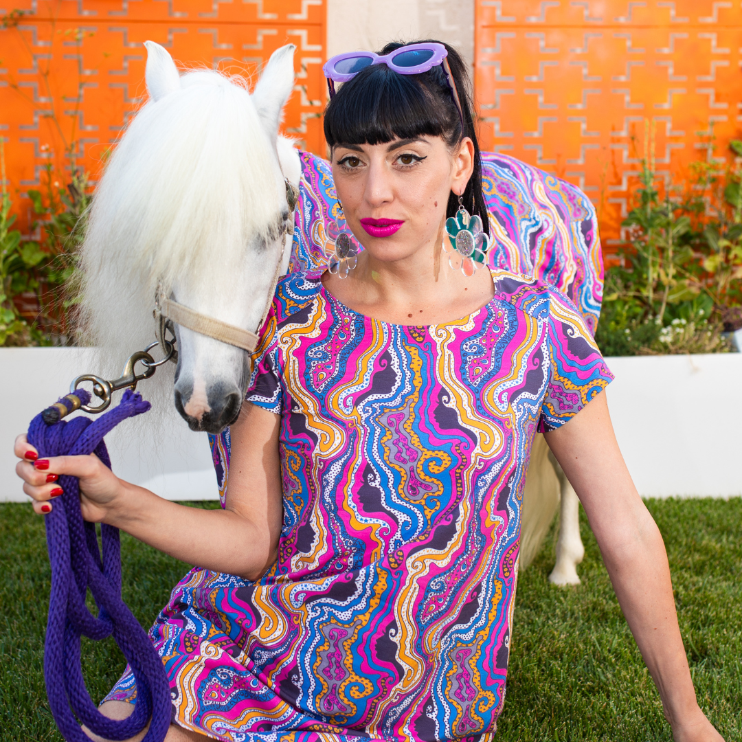 Closeup of stunning dark haired model and white mini horse in bright psychedelic print clothing