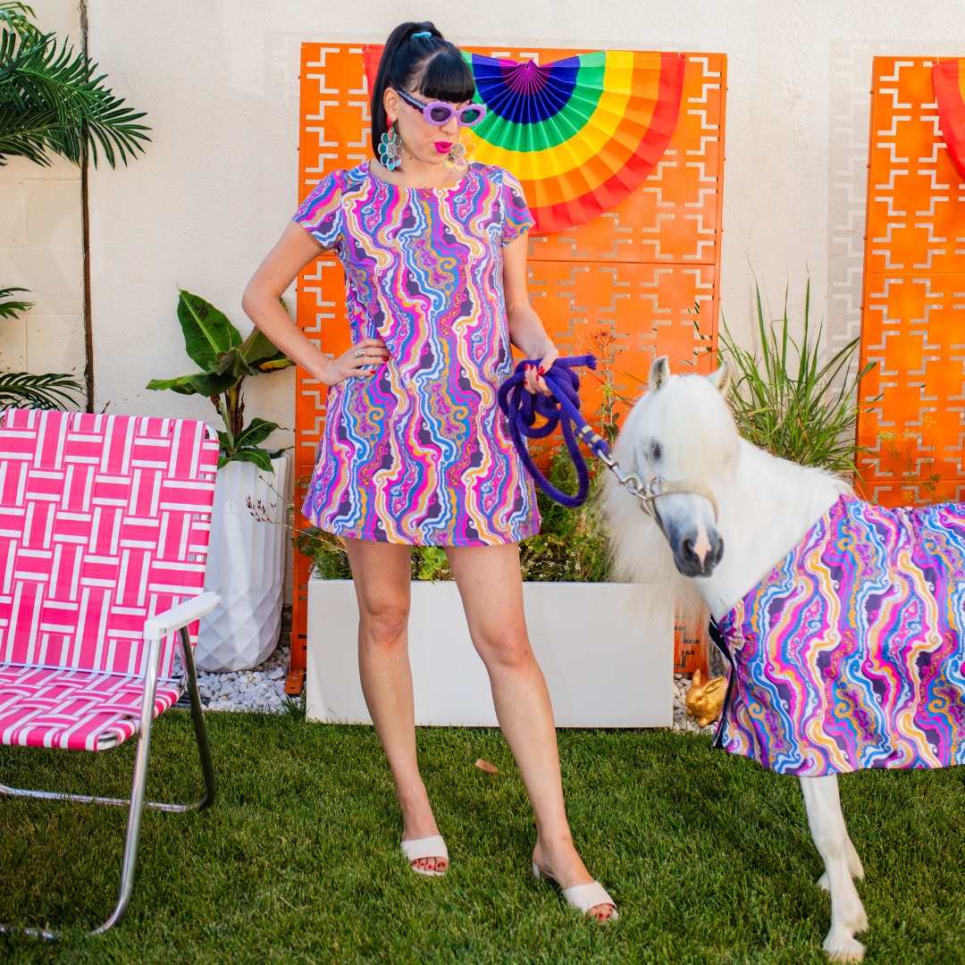 Tall dark-haired model in colorful psychedelic mini tunic dress with matching mini horse