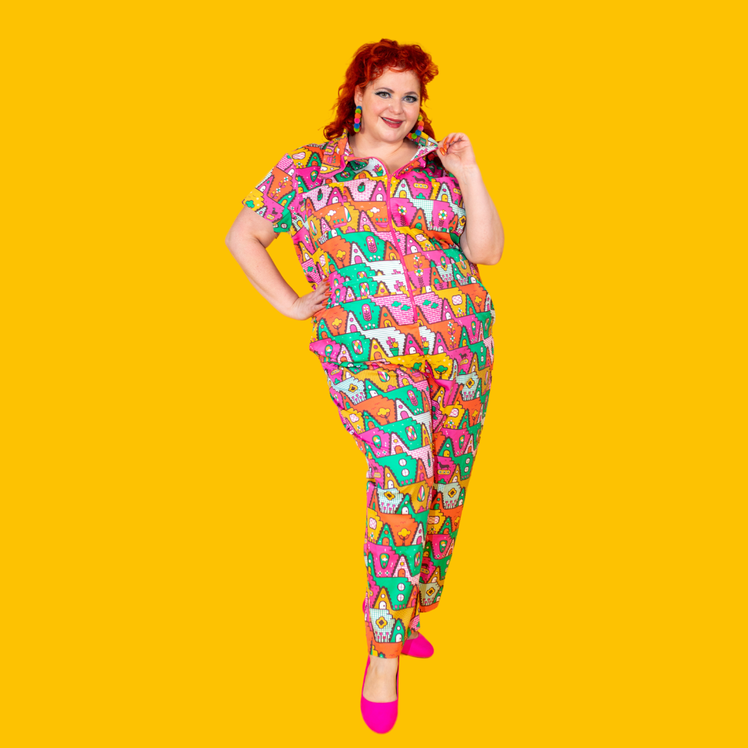 Red-haired model in bright colored geometric print jumpsuit of houses, pets and quirky elements