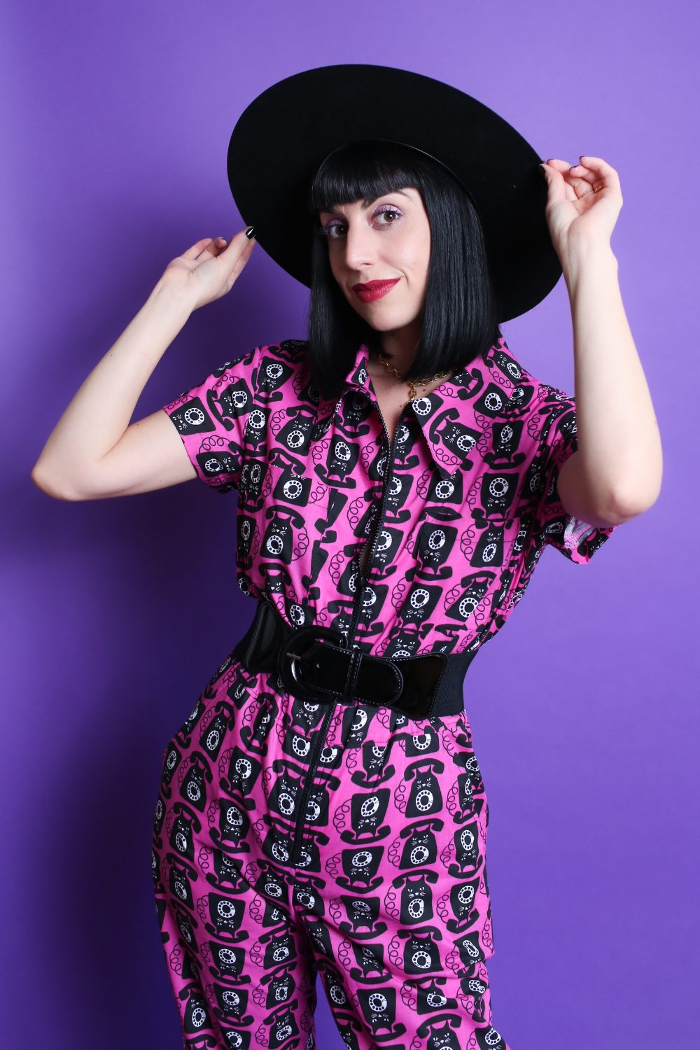 Black haired model in black hat and pink and black printed jumpsuit