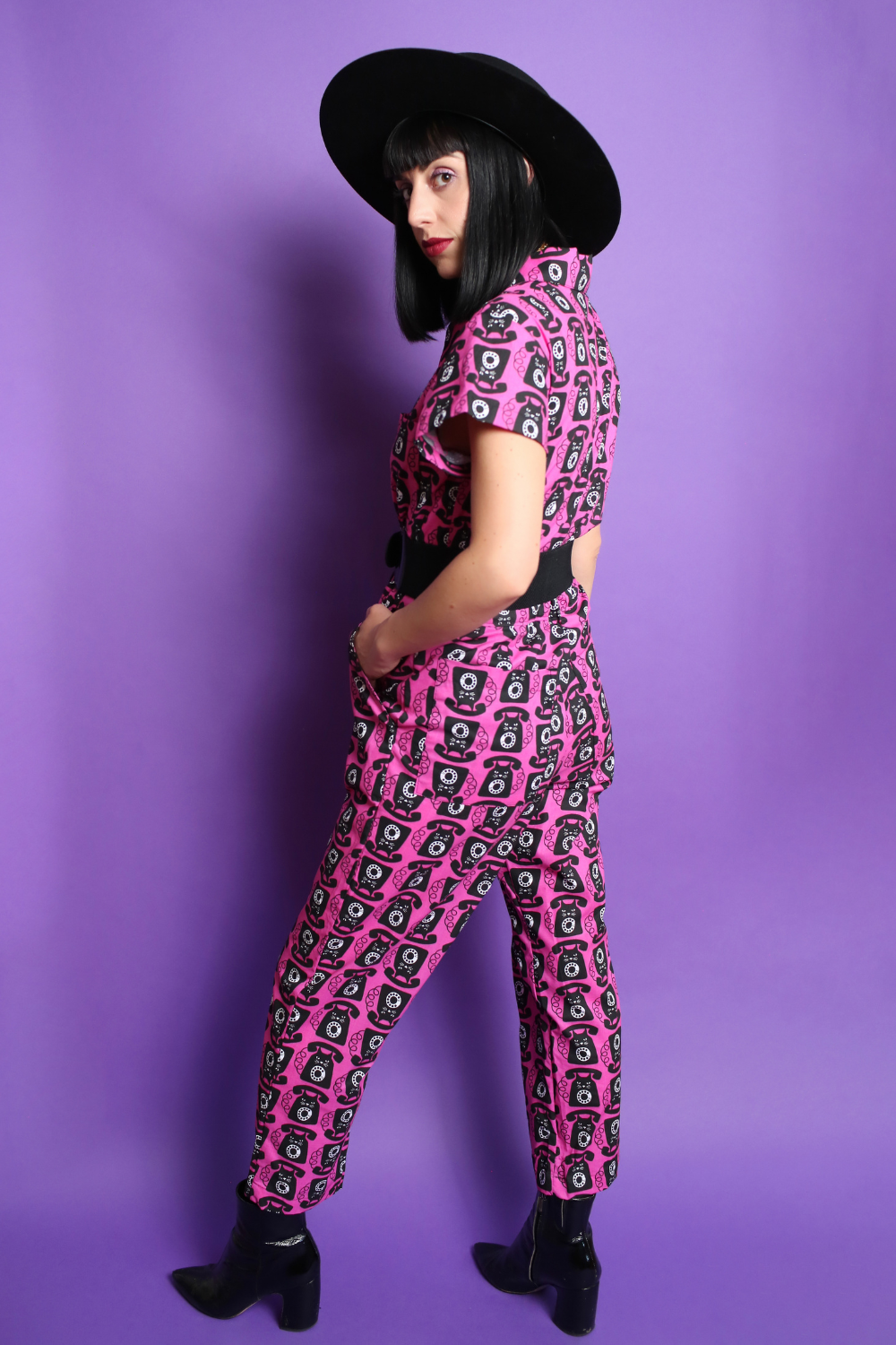 Black haired model in black hat and pink and black printed jumpsuit, back view