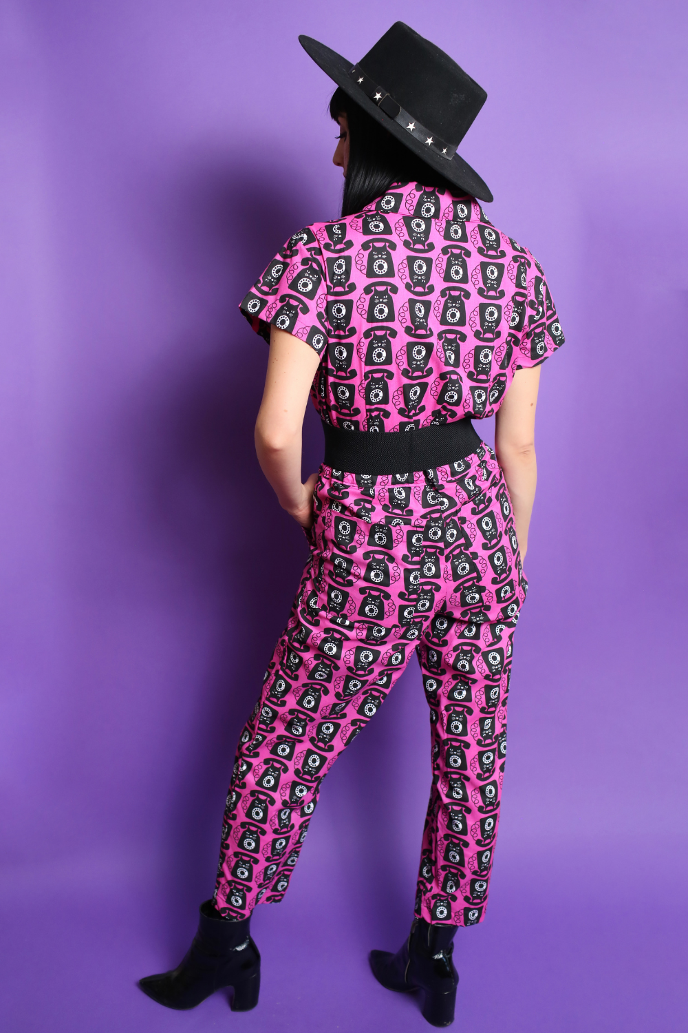 Black haired model in black hat and pink and black printed jumpsuit