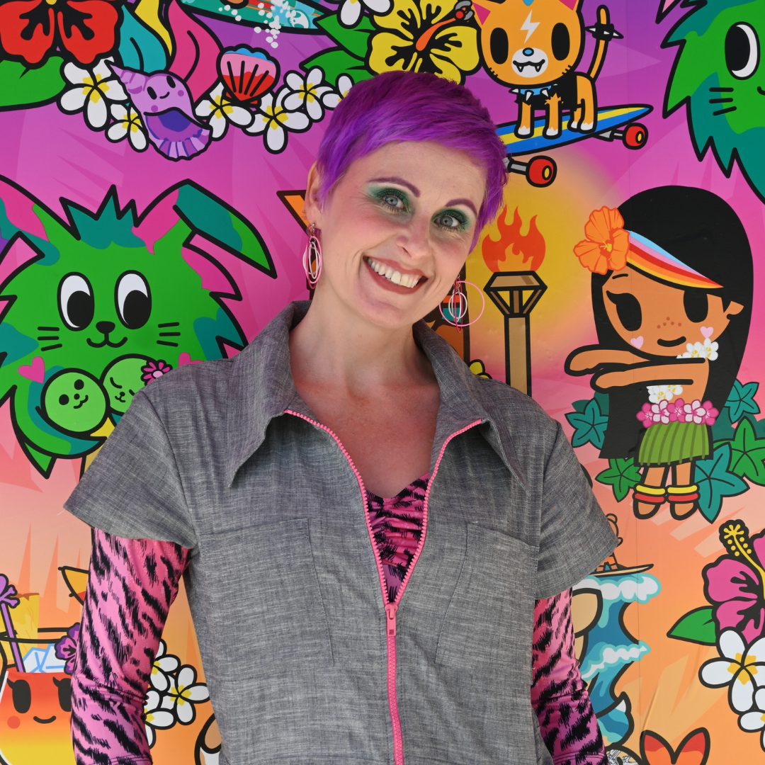 Closeup of purple-haired model in chambray jumpsuit with pink zip and pink animal print shirt