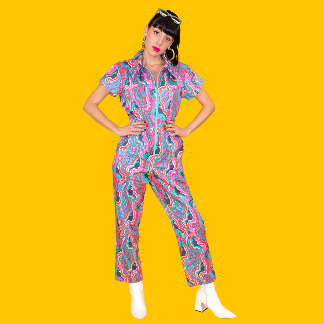 Full-body view of dark-haired model in psychedelic jumpsuit with fun zipper and white boots