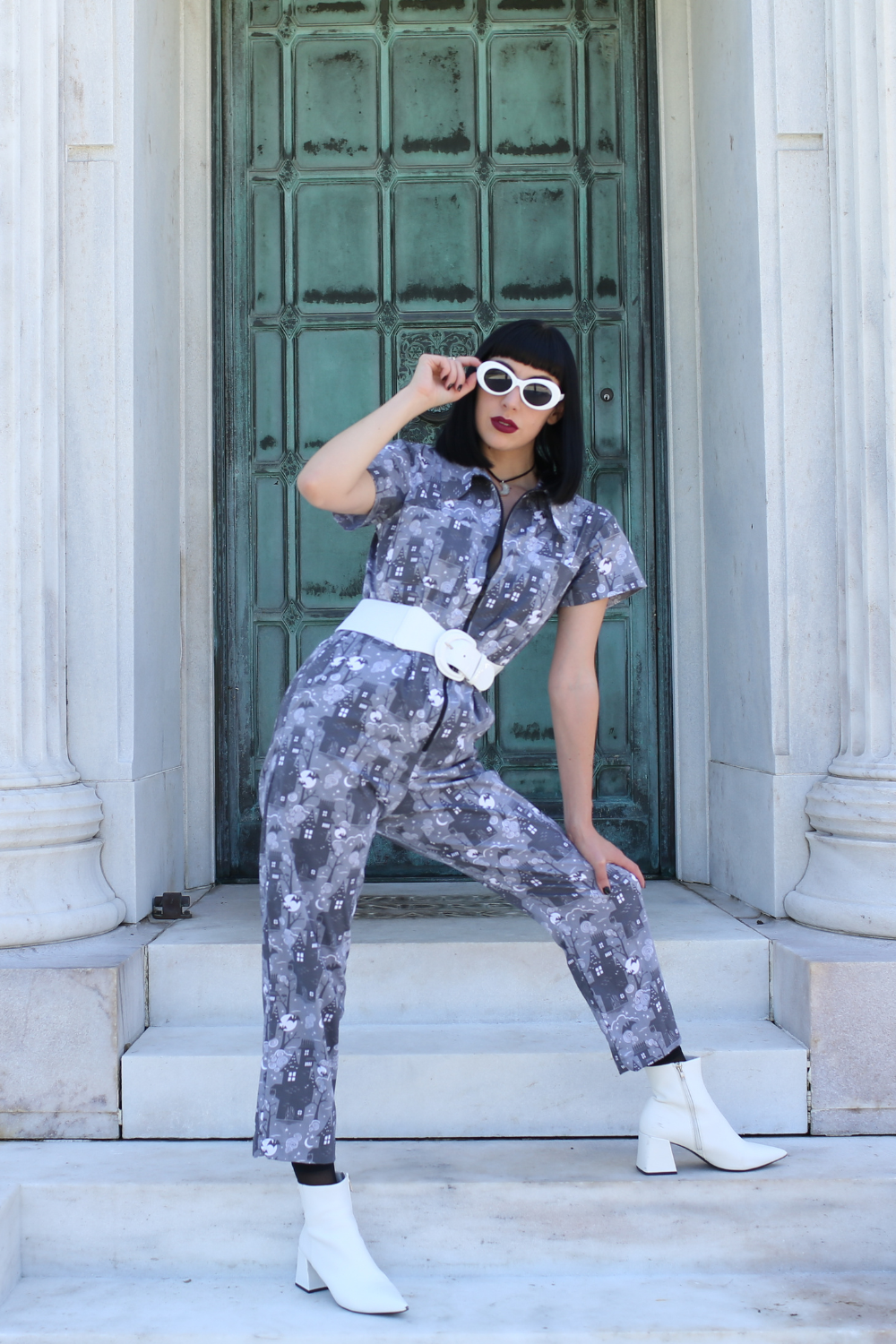Tall model wearing grey haunted house print jumpsuit with white accessories
