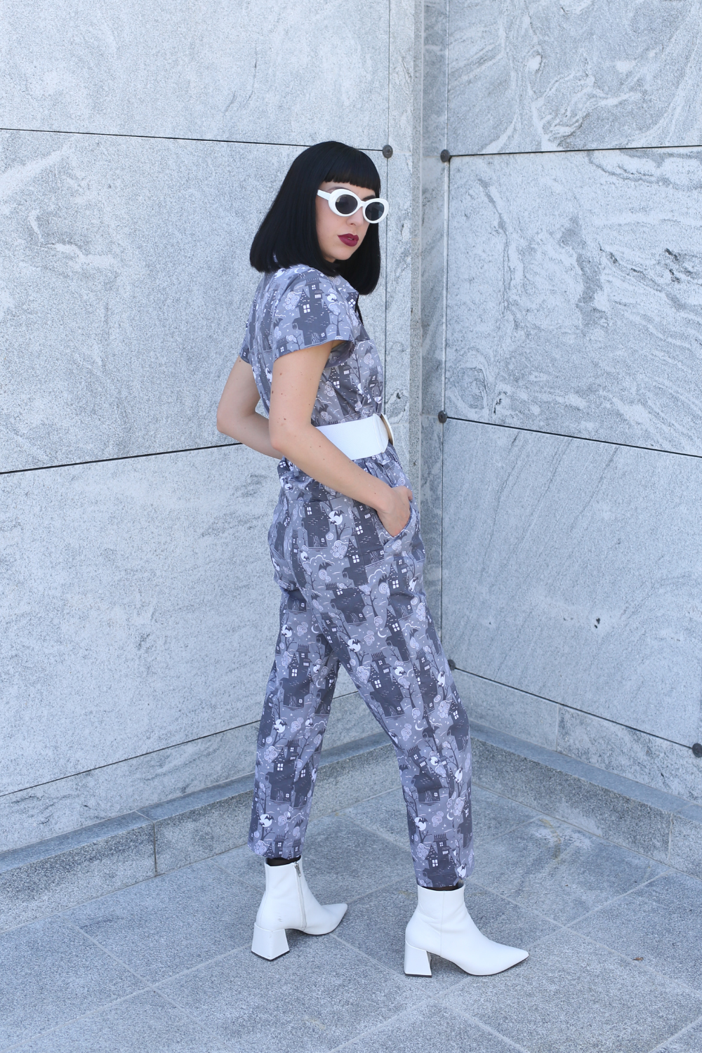 Tall model wearing grey haunted house print jumpsuit with white accessories, side view