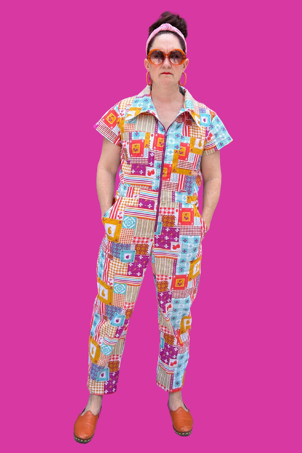 Model wearing sunglasses and patchwork print zip-front collared jumpsuit on pink background