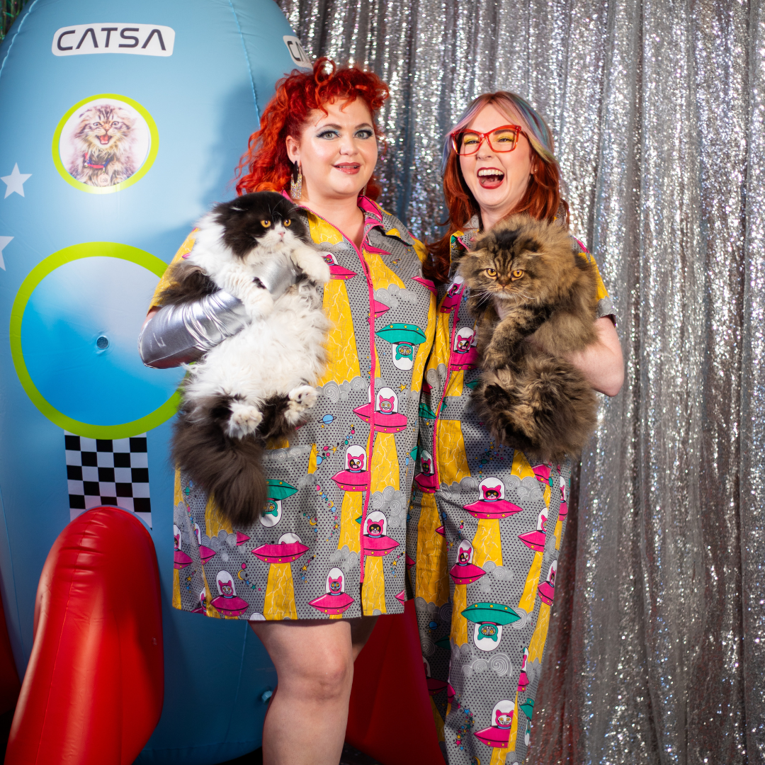 2 models having fun holding cats and wearing clothing in a fun print of cats in spaceships