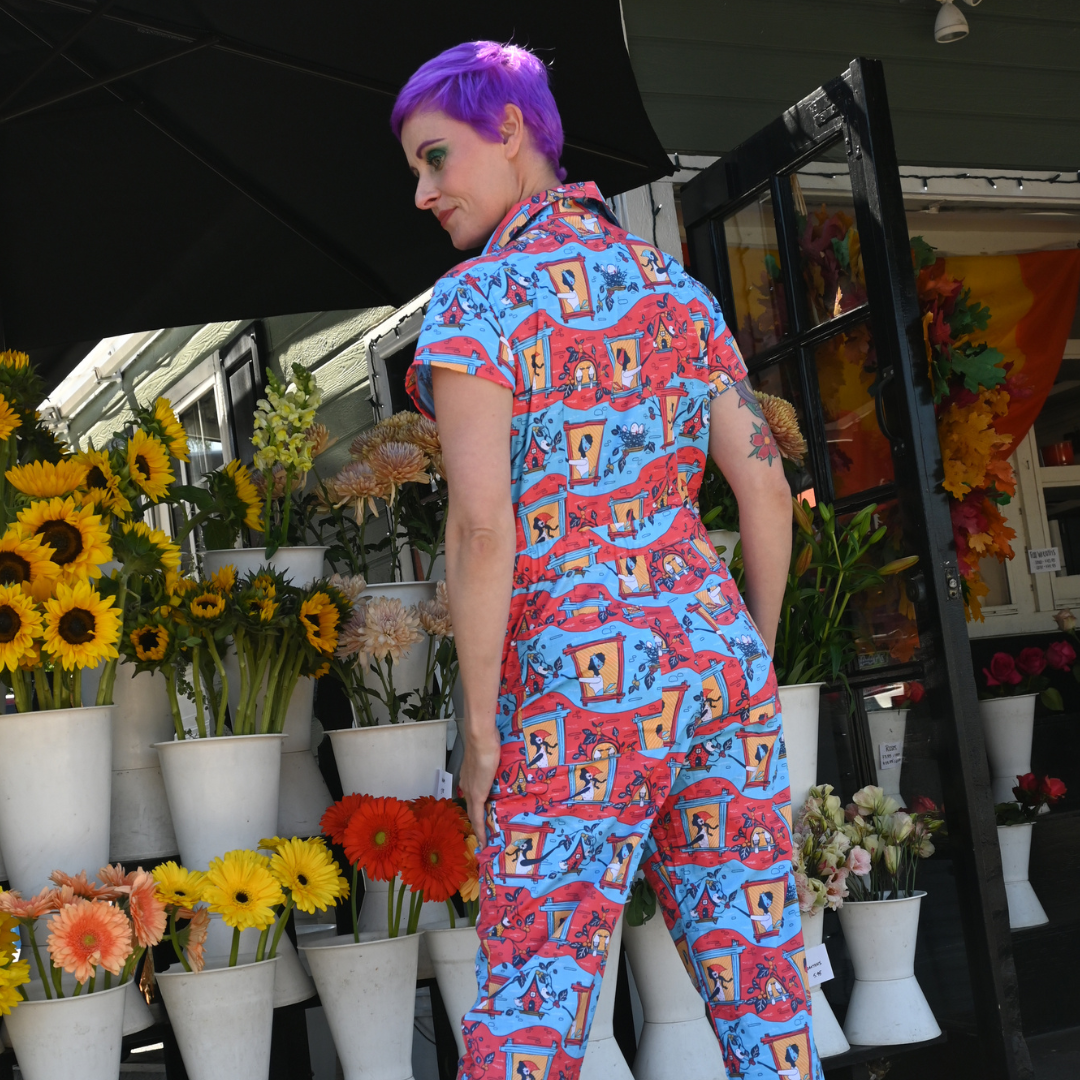 Purple-haired model in red, yellow and blue jumpsuit with girls in windows print, back view