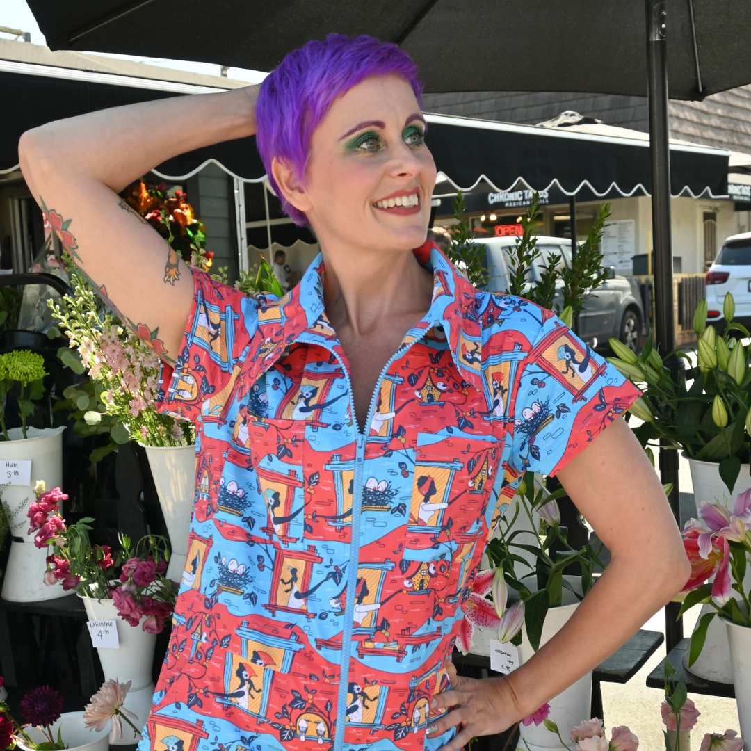 Closeup of purple-haired model in red, yellow and blue coveralls with print of girls and birds nests