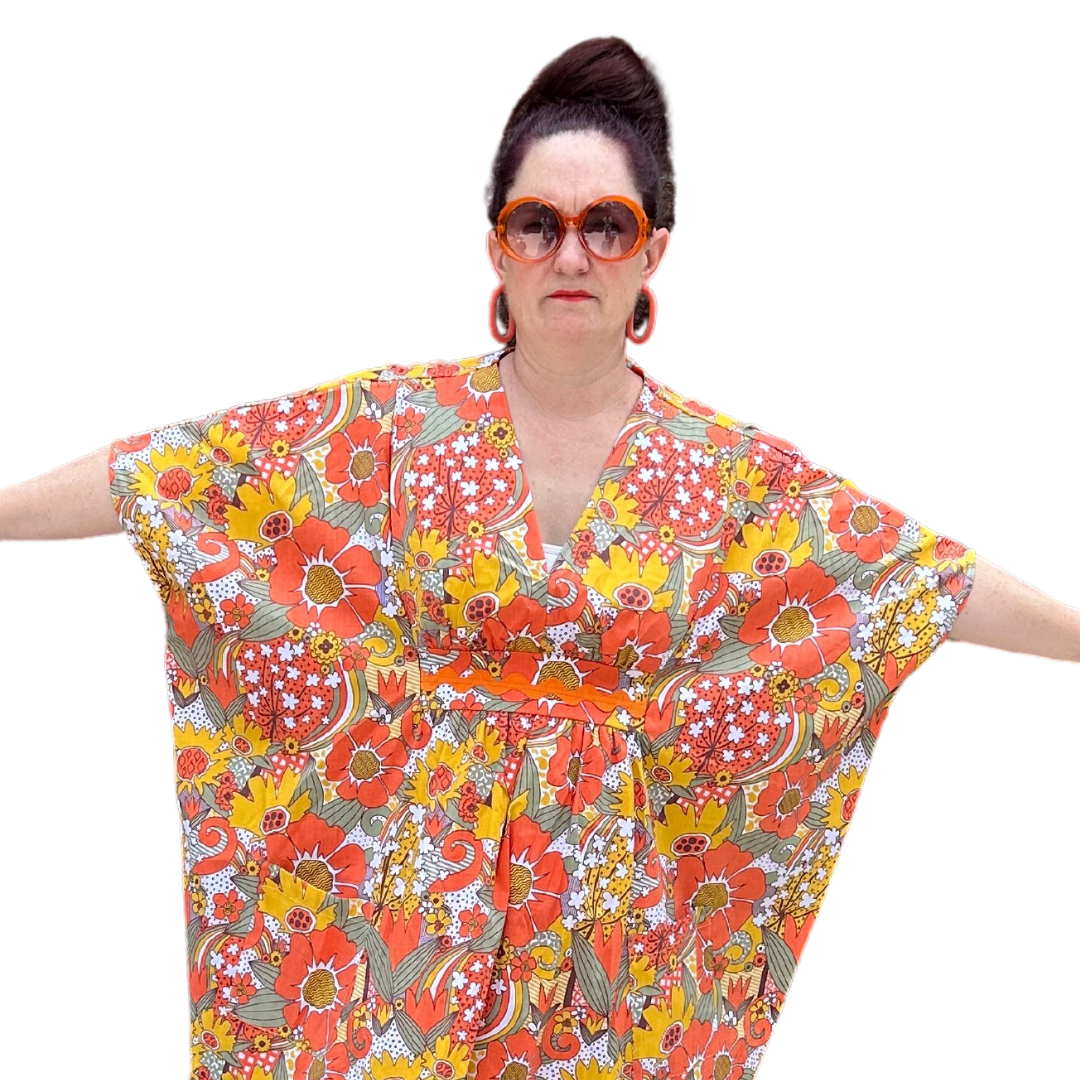 Closeup of brown-haired model wearing sunglasses and bright floral print caftan 