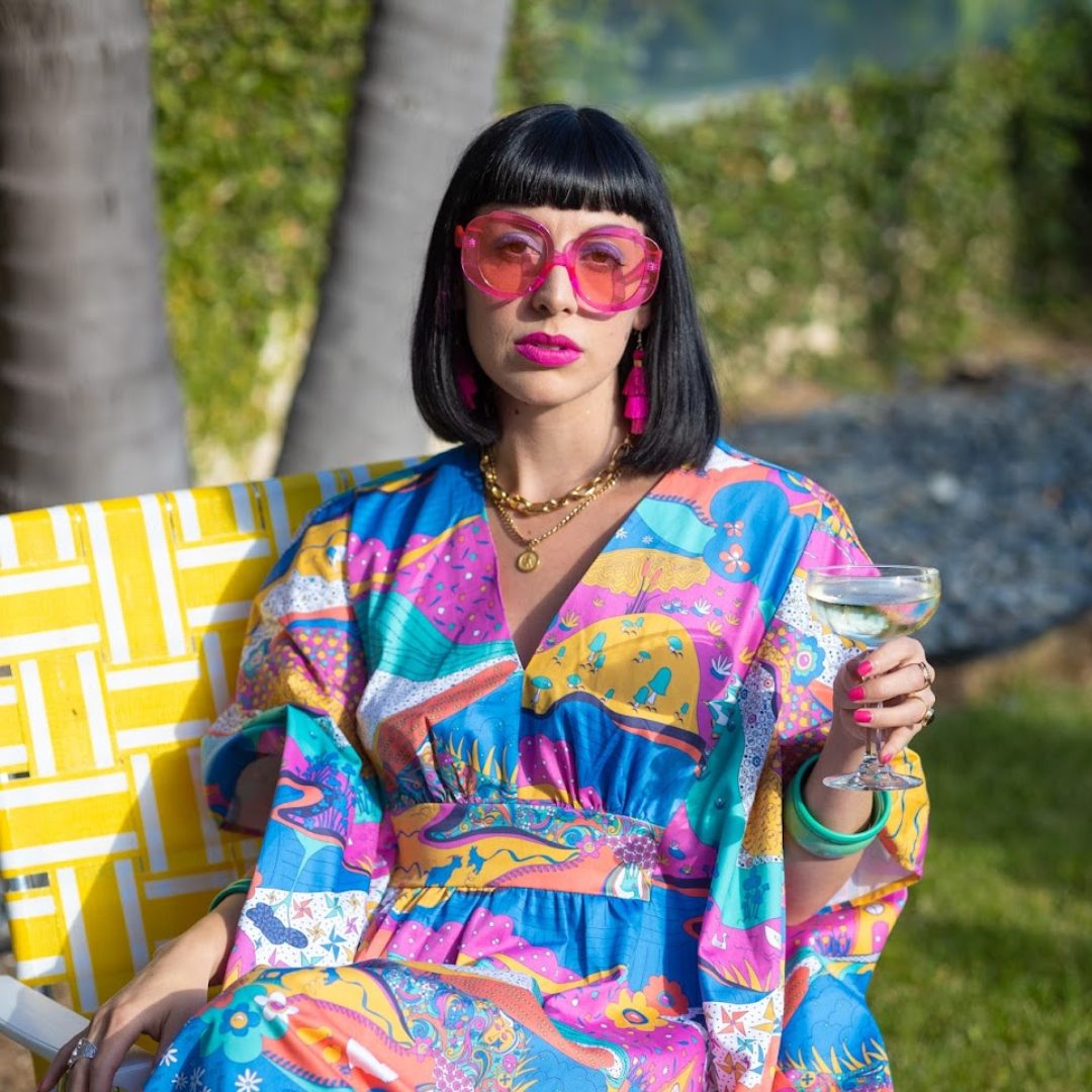 Black-haired model in colorful caftan sunning herself in a lawn chair with a cocktail