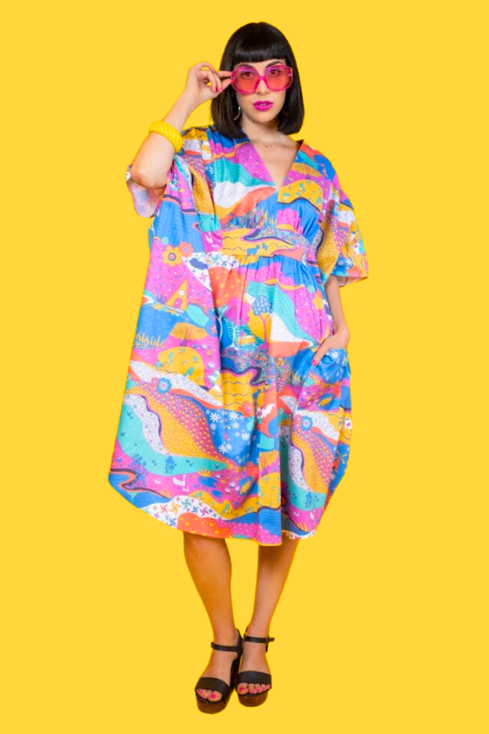 Pretty dark-haired model in big sunglasses and colorful landscape print caftan