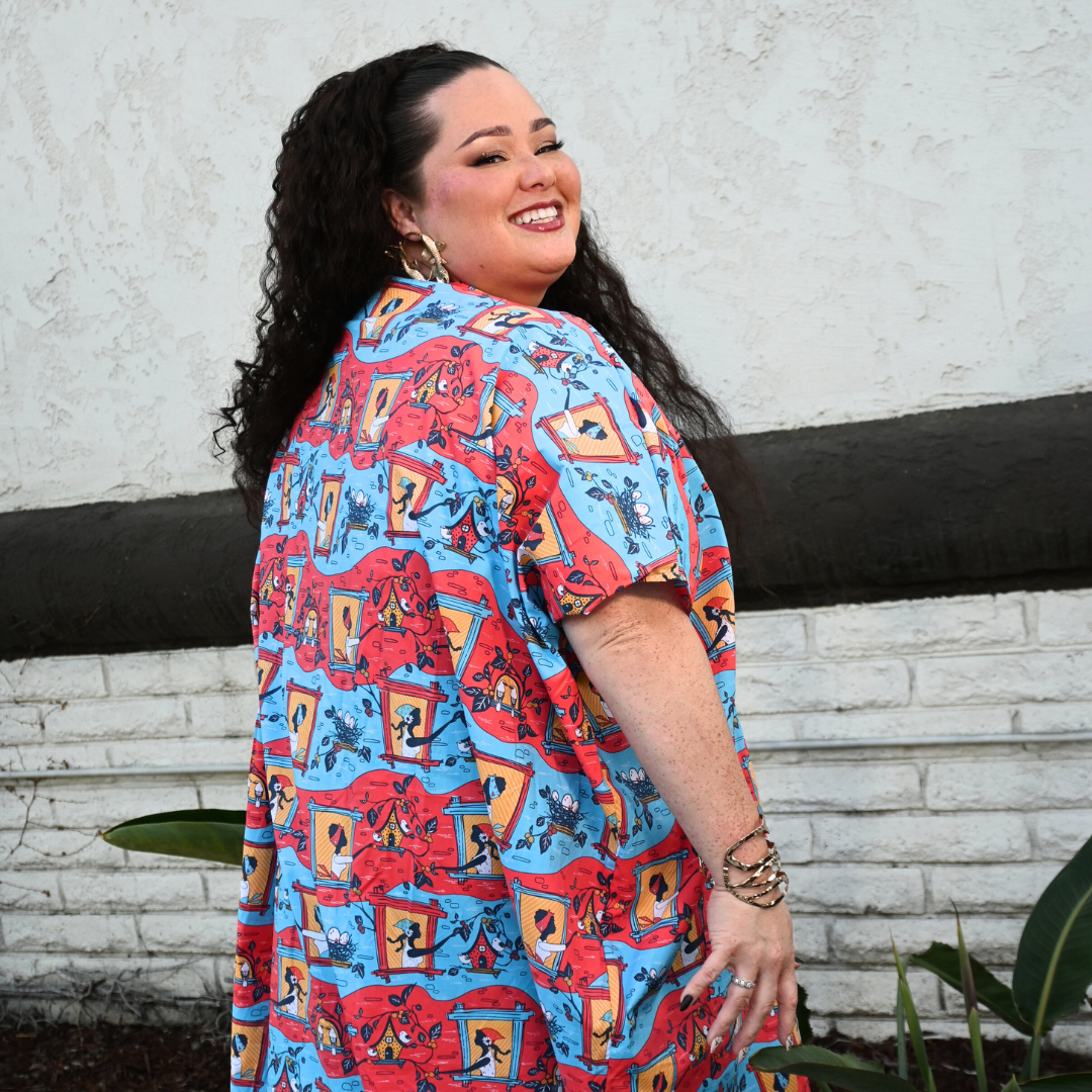 Dark-haired model in red and blue caftan with print of women and bird, back view