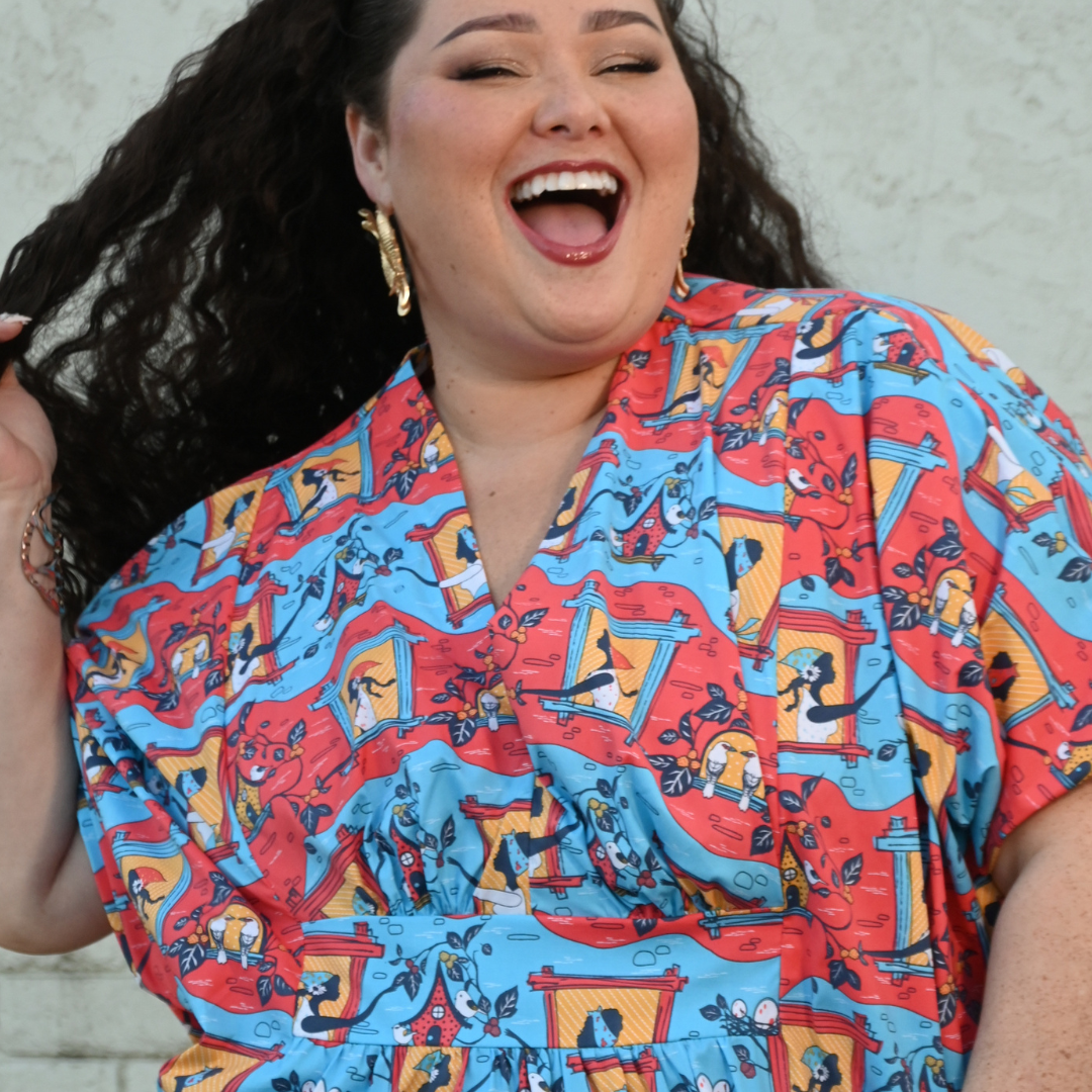 Closeup of dark-haired model in red and blue caftan with print of women and birds