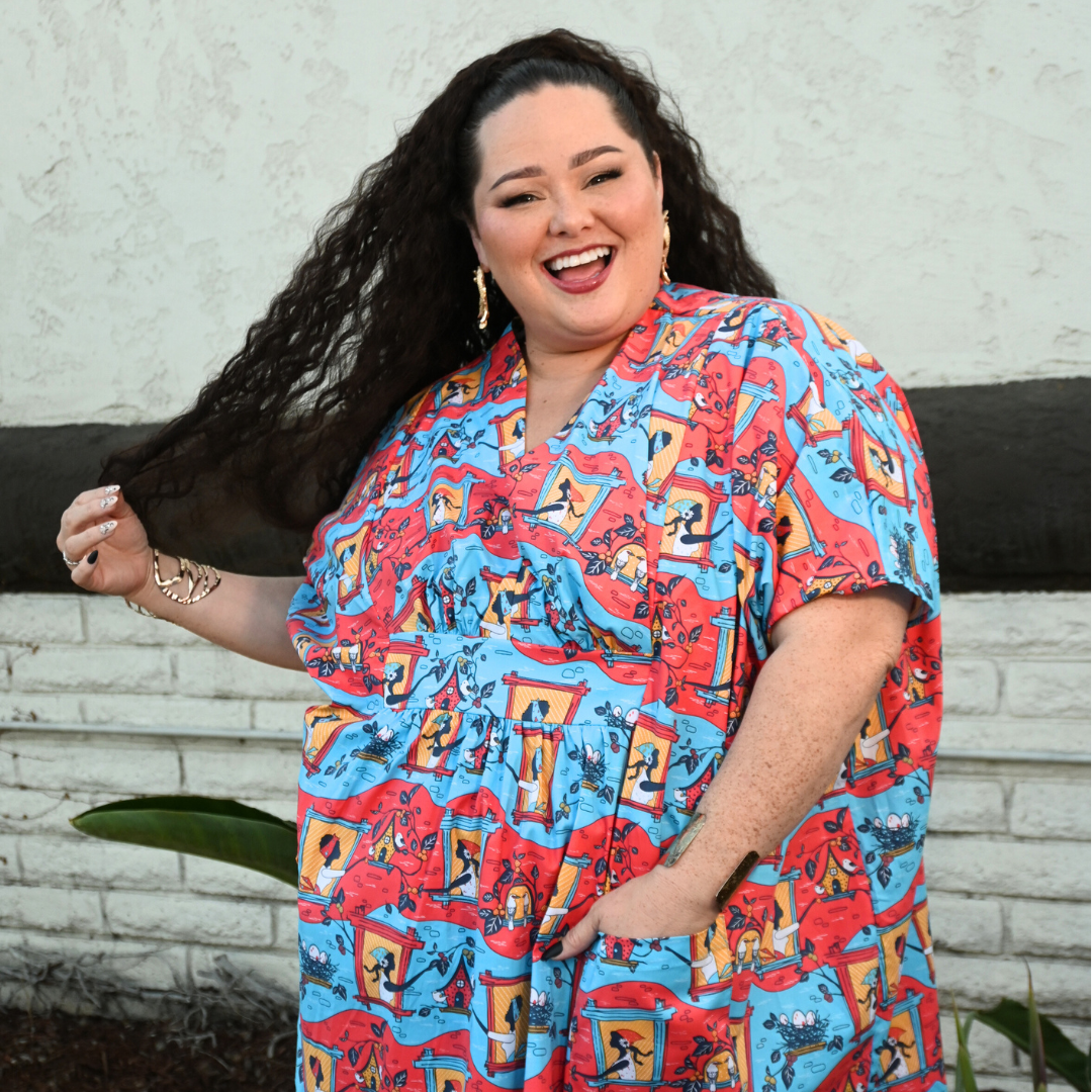 Dark-haired model in red and blue caftan with print of women, birds and birds nests